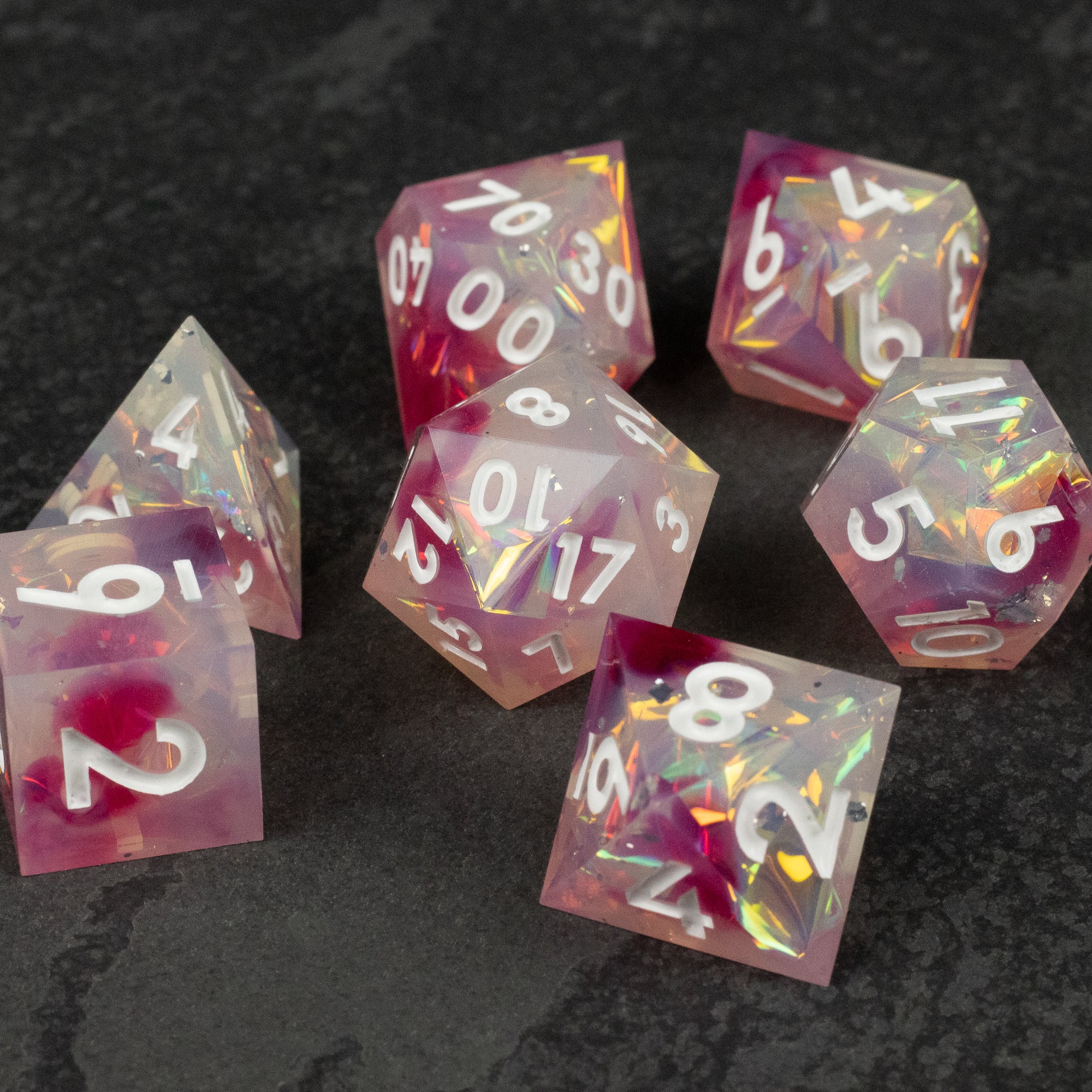 Lover's Kiss Dice Set - Translucent pink and purple polyhedral dice with sharp edges and white numbers, containing gold and iridescent flakes inside.