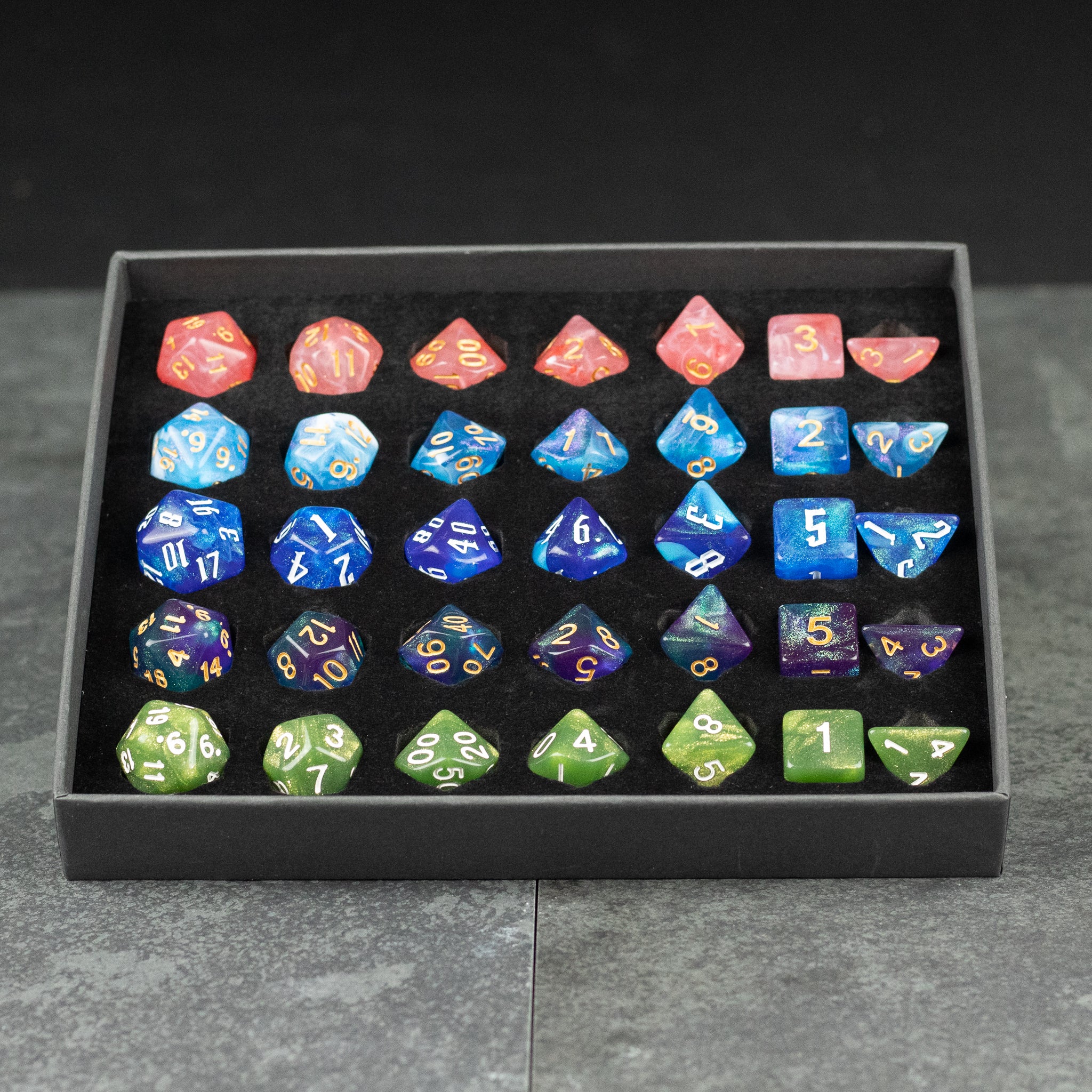 Acrylic Dice Set Gift Box - Set of 36 acrylic polyhedral dice in red, blue, purple, and green with white and gold numbers, displayed in black tray.