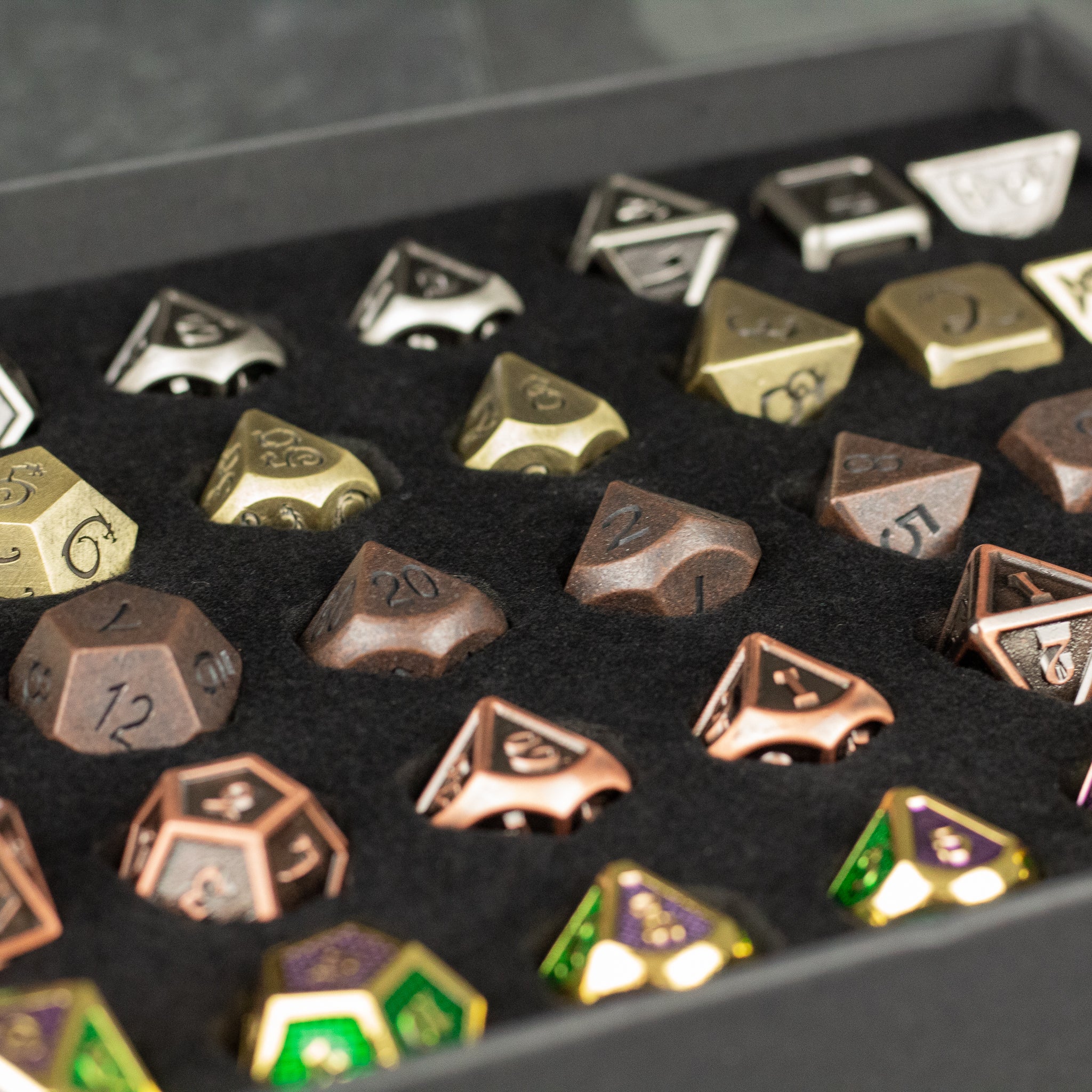 Metal Dice Set Gift Box - Metal multi-sided dice in silver, gold, bronze, and green with black numbers neatly arranged in black foam.