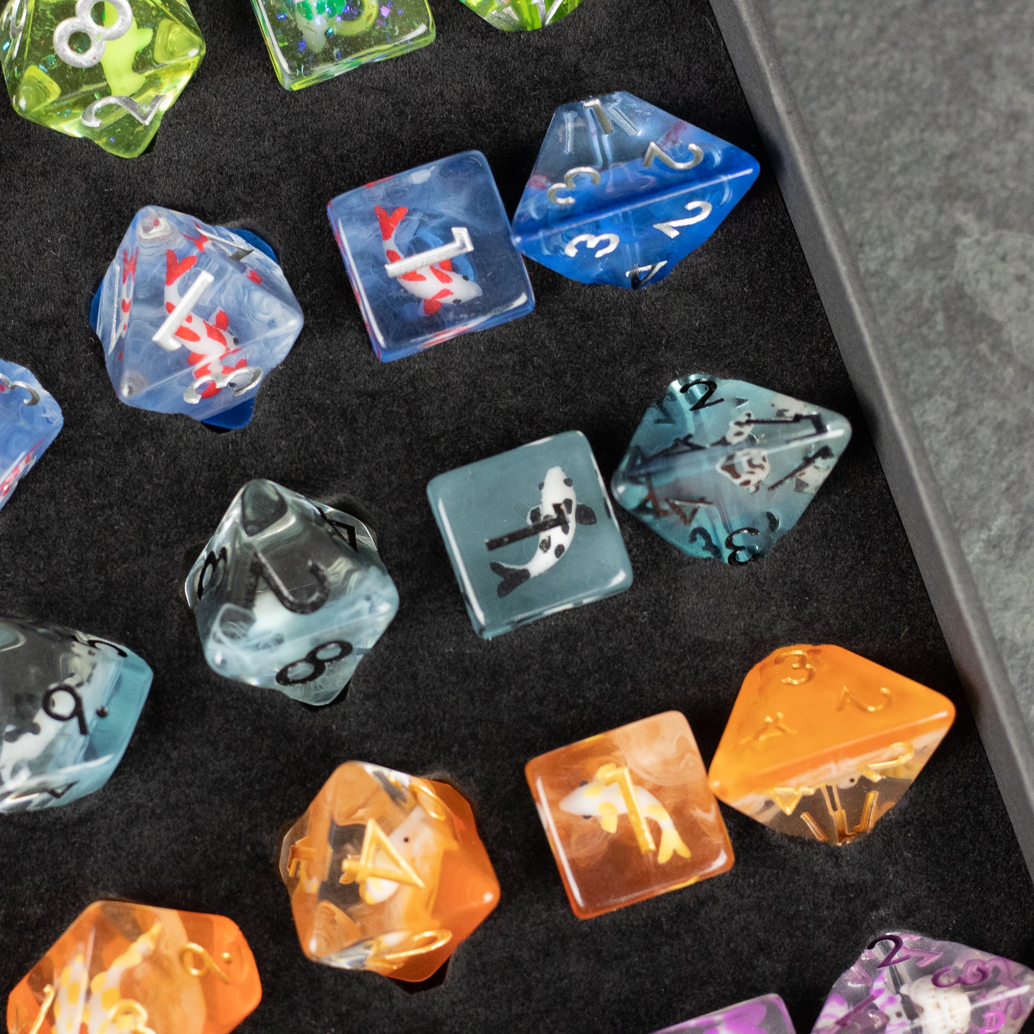Koi Fish Dice Set Gift Box - Set of translucent polyhedral dice in blue, black, orange, and purple with koi fish designs inside, displayed on black.