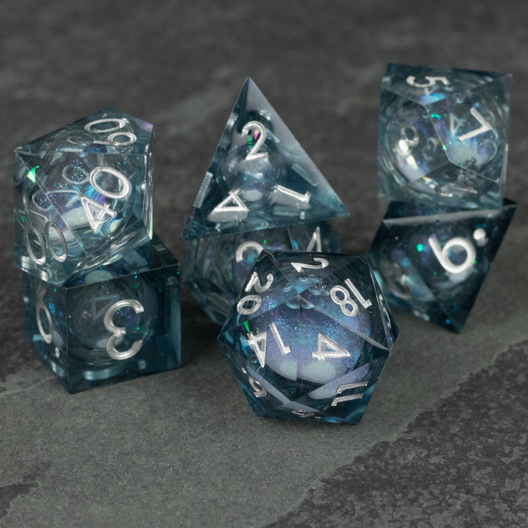 Astral Sea Liquid Core Dice Set - Set of six transparent black liquid core dice with sharp edges and white numbering on dark gray stone surface.