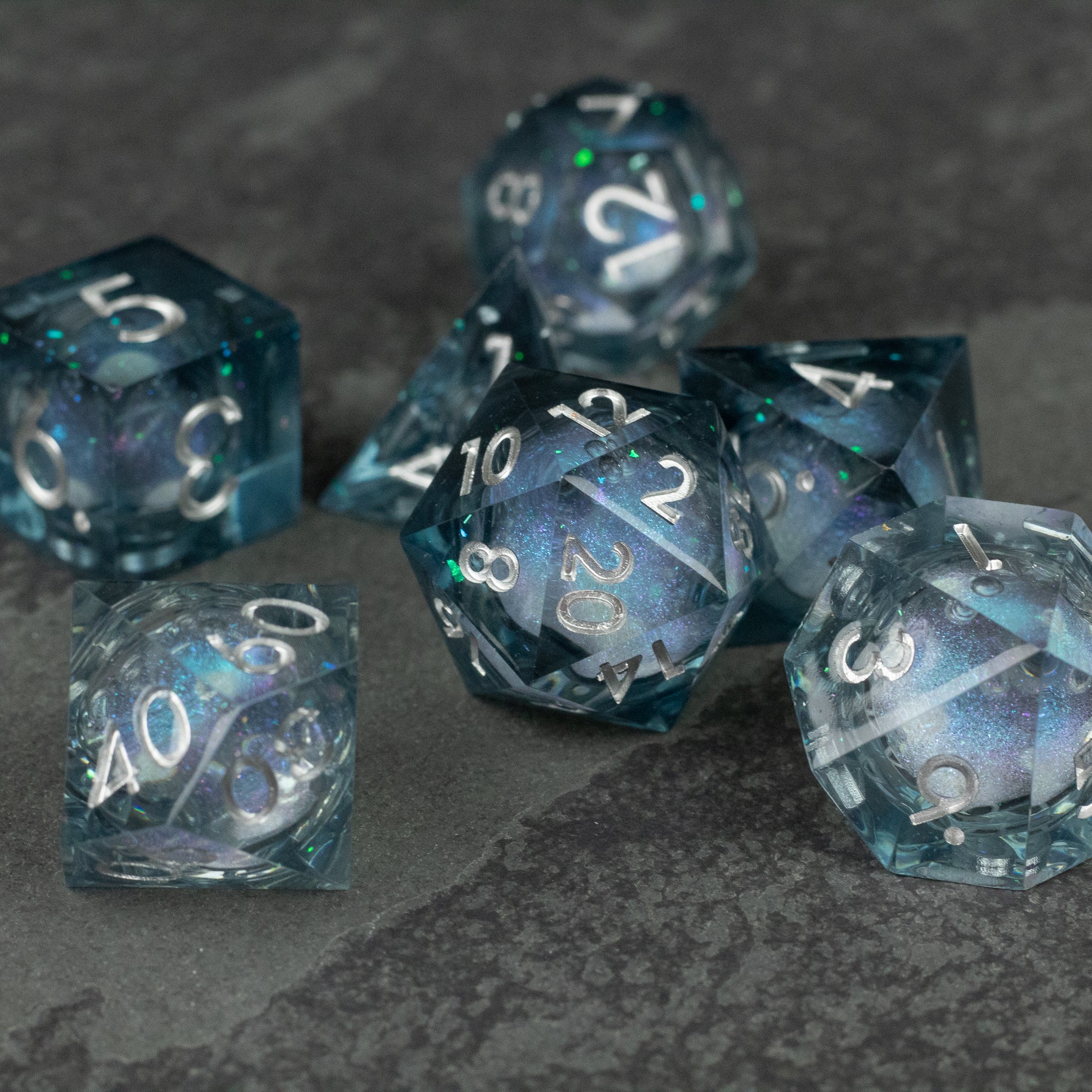 Astral Sea Liquid Core Dice Set - Set of seven translucent blue-green sharp-edged polyhedral dice with white numbers and swirling liquid core design.