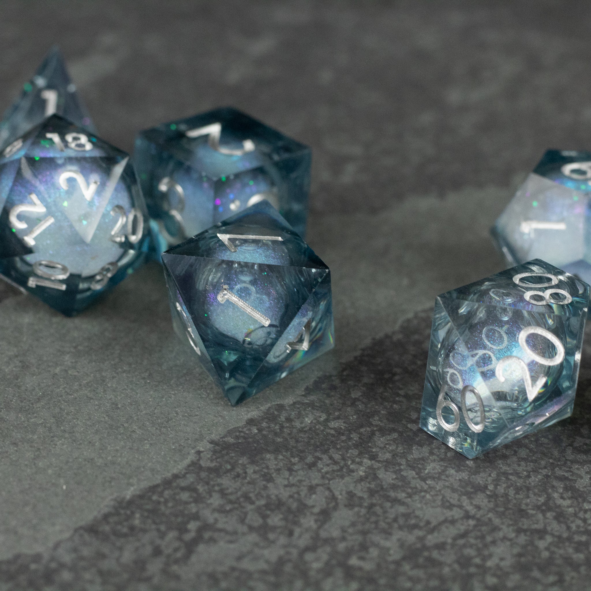 Astral Sea Liquid Core Dice Set - Set of translucent sharp-edged dice with deep blue and silver swirling liquid core featuring white numbering.