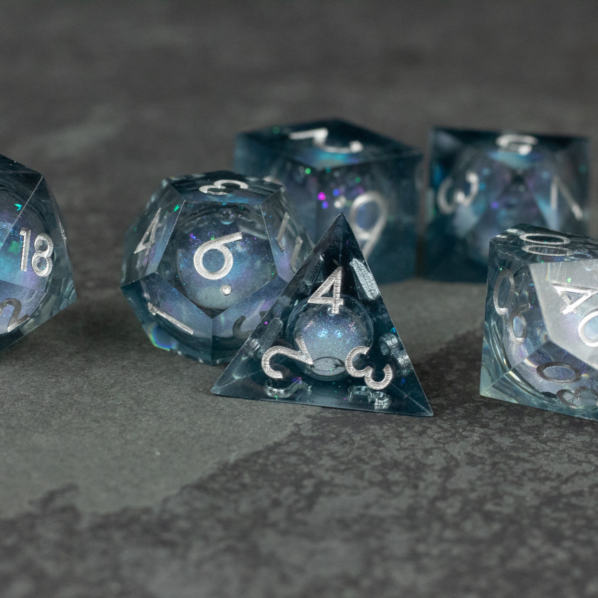 Astral Sea Liquid Core Dice Set - Translucent blue liquid core sharp-edged dice set with white numbering, including d20, d12, d10, and d4 shapes.