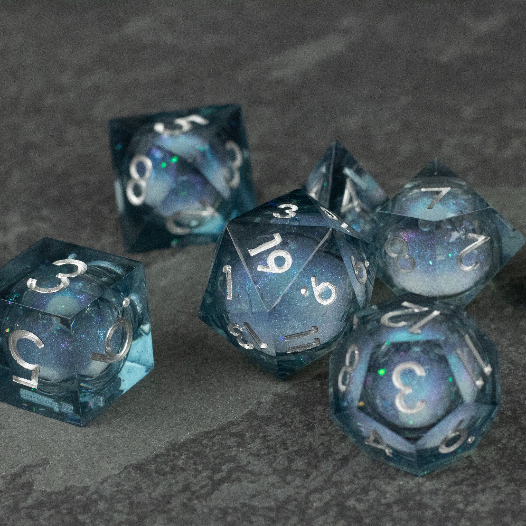 Astral Sea Liquid Core Dice Set - Set of six translucent blue polyhedral dice with swirling iridescent liquid cores and sharp edges, white numbering.