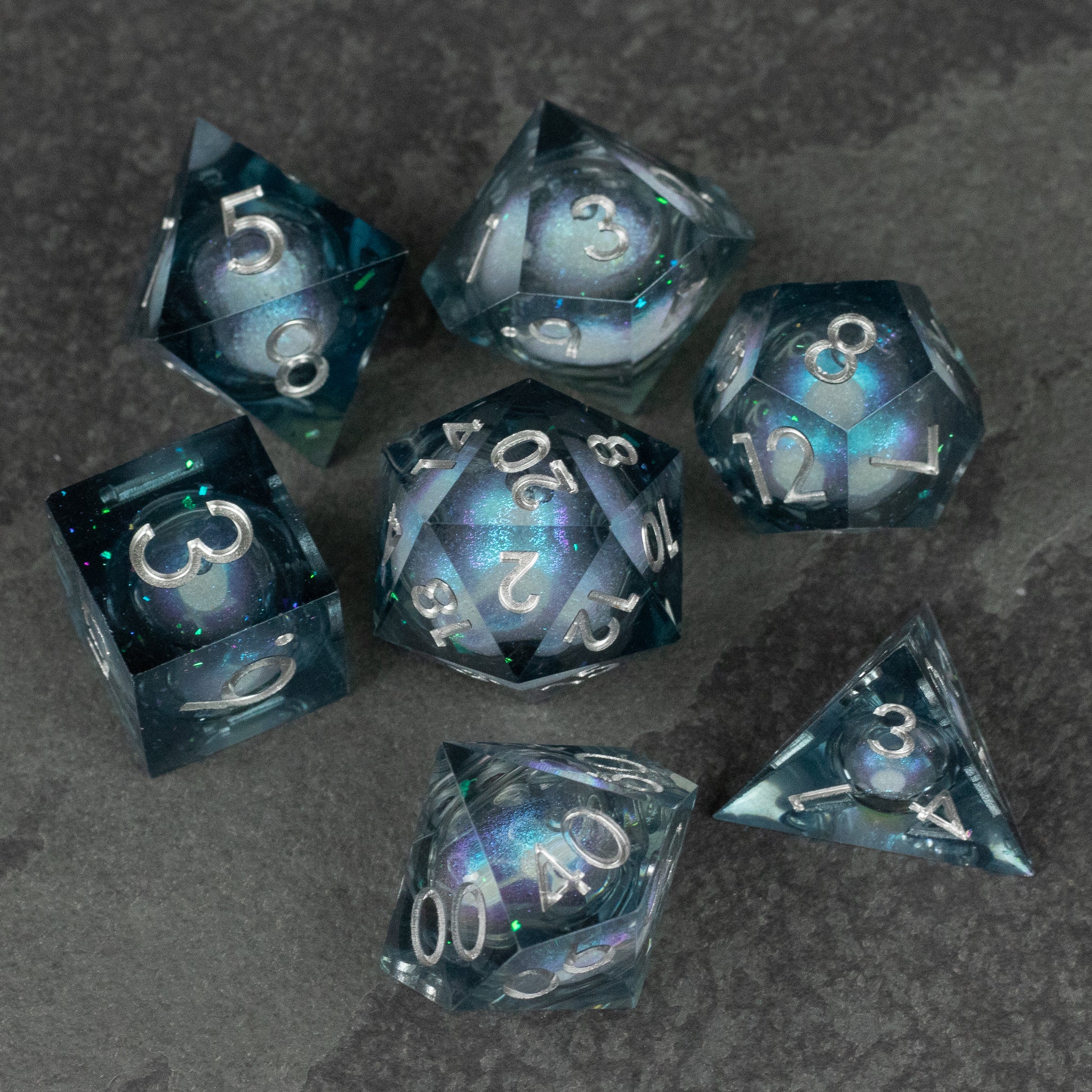 Astral Sea Liquid Core Dice Set - Set of seven sharp-edged blue liquid core dice with silver numbers on a dark surface.