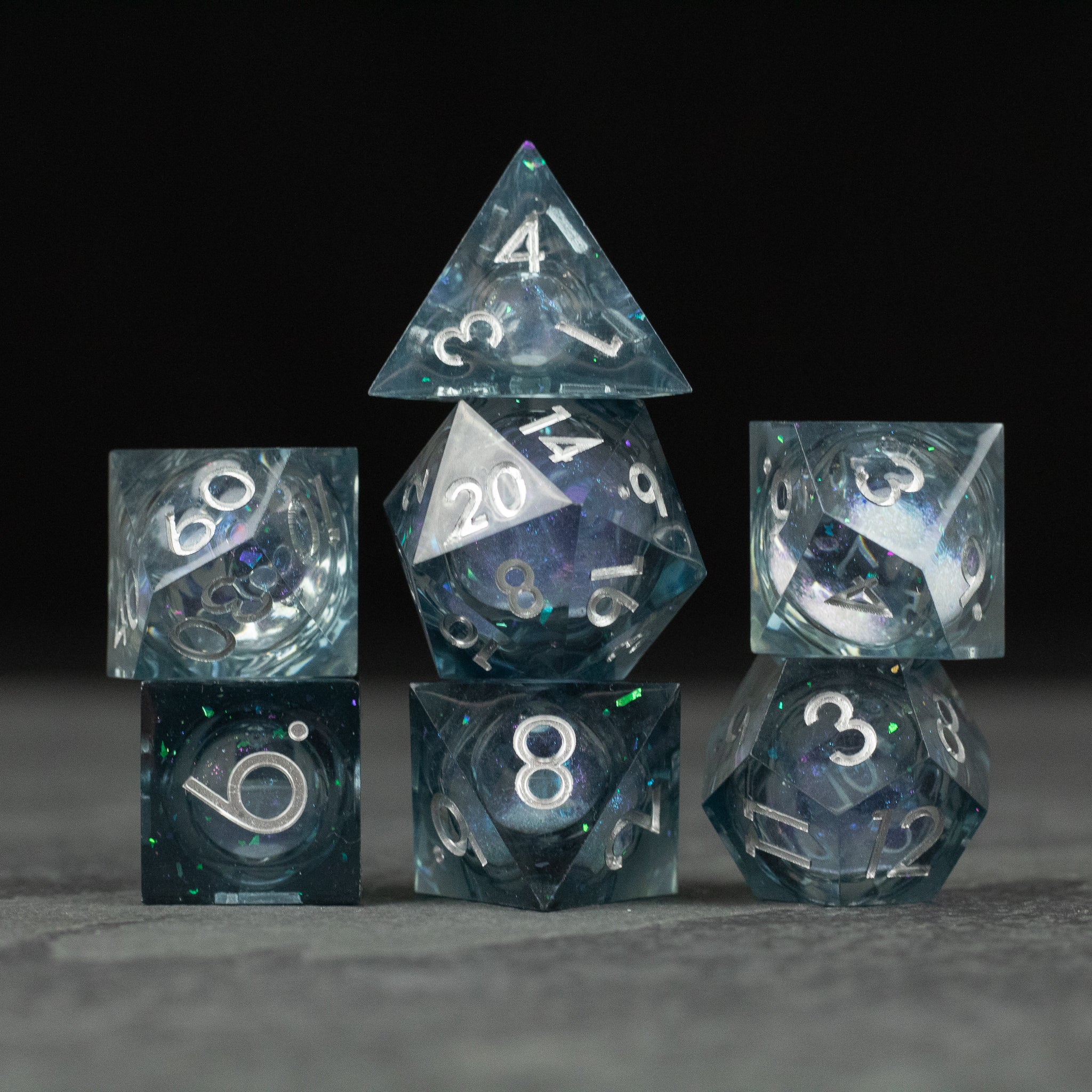 Astral Sea Liquid Core Dice Set - Set of seven transparent polyhedral dice with sharp edges, containing swirling blue and white liquid core and white.