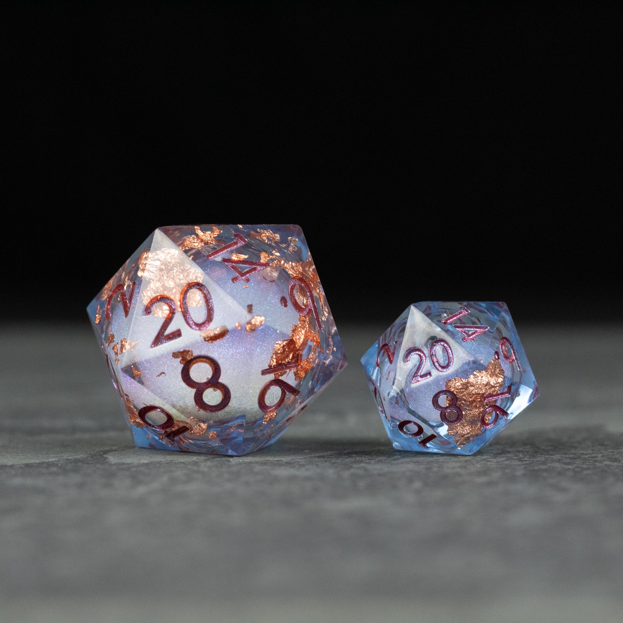 33mm Liquid Core D20 Chonk - Blue + Foil - Large and small blue 20-sided dice with copper foil inclusions and metallic numbers on a dark surface.