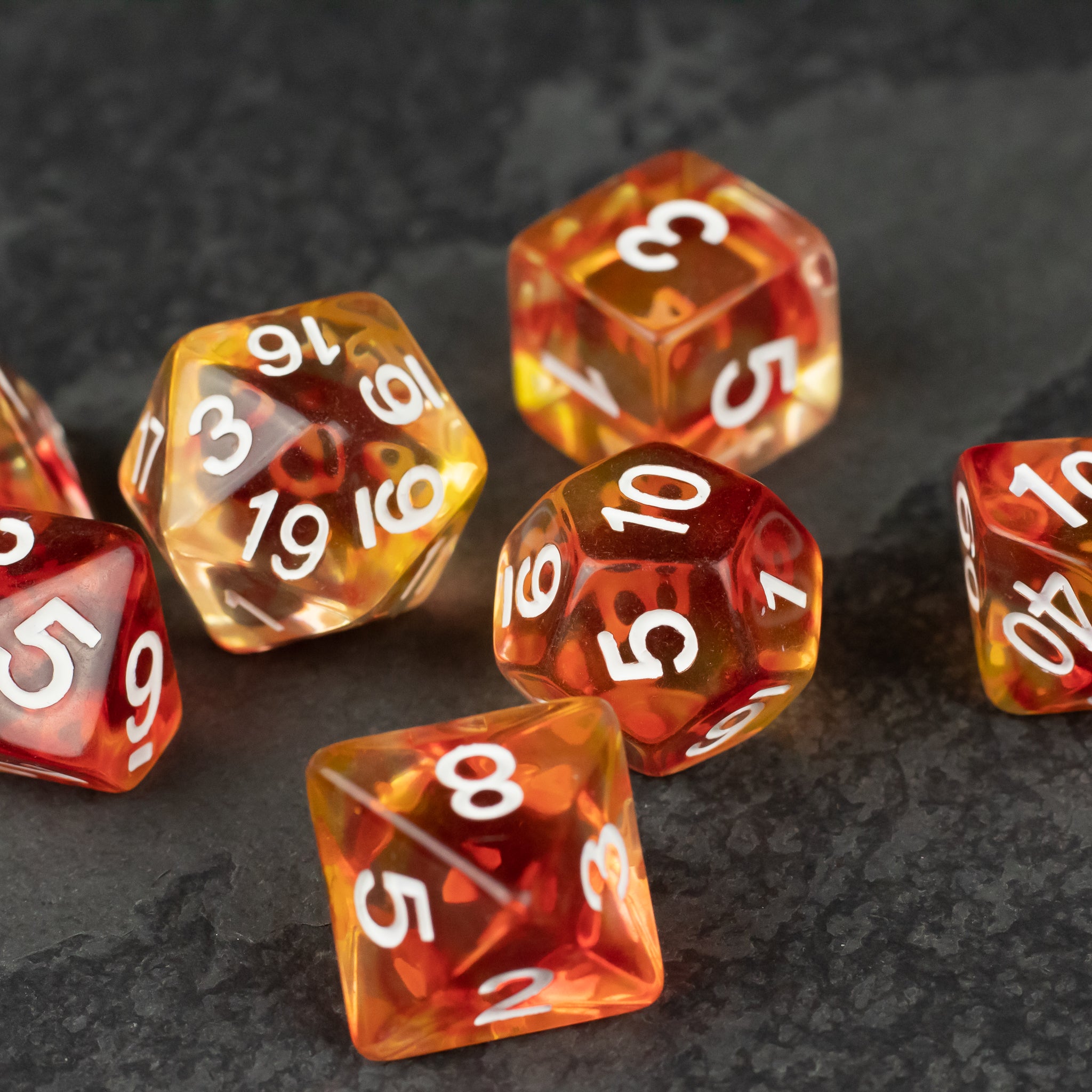 Magma Dice Set - Transparent orange-red polyhedral dice set with white numbering, including d20, d12, d10, and d8 shapes on a dark surface.