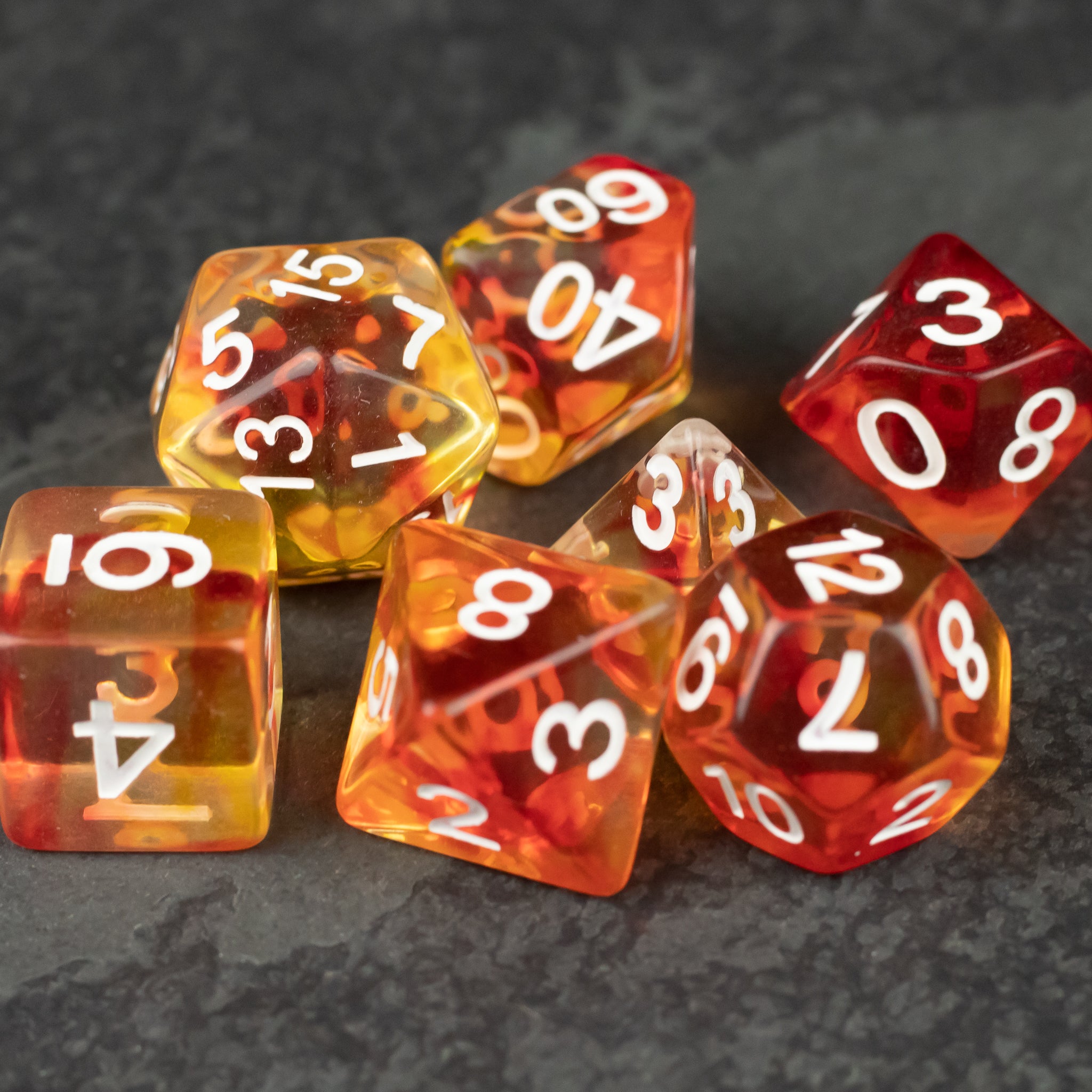 Magma Dice Set - Translucent orange-red polyhedral dice set with white numbers on a dark gray surface.