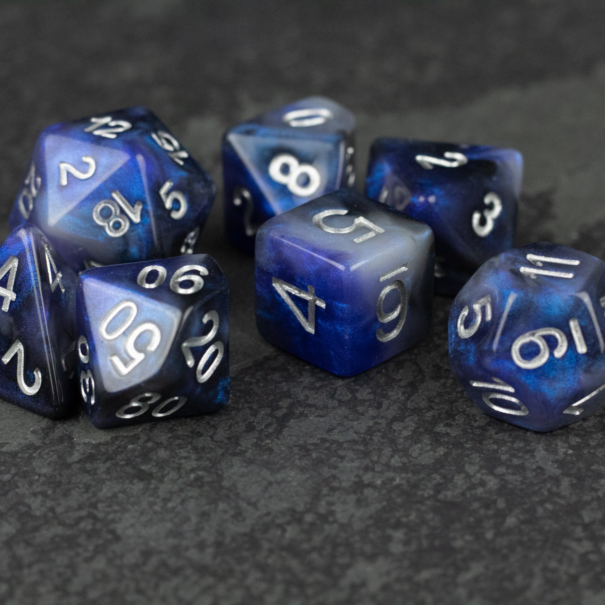 Cosmic Dust Dice Set - Set of seven polyhedral dice in blue and black cosmic swirl design with white numbering.