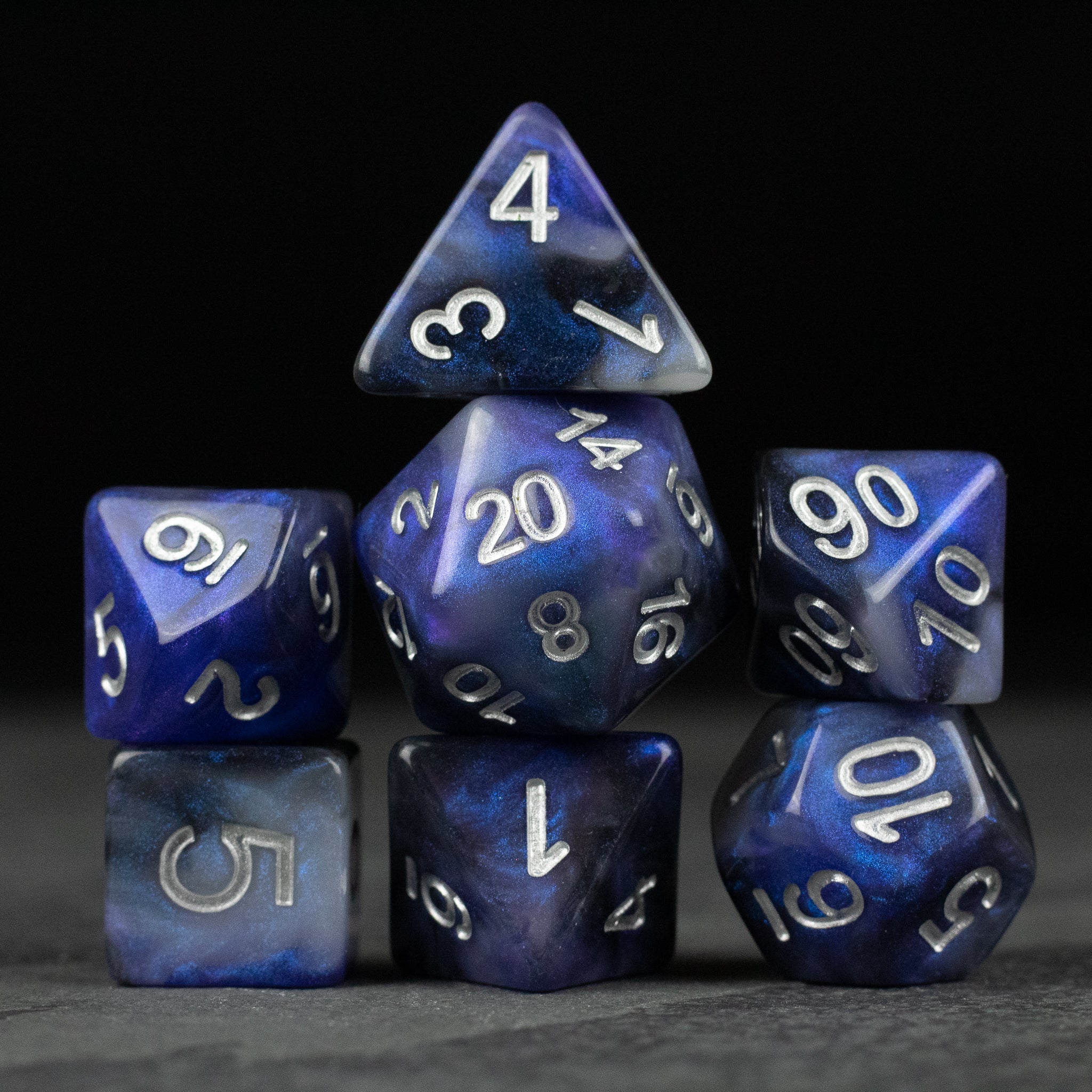 Cosmic Dust Dice Set - Seven-piece blue cosmic-themed polyhedral dice set with white numbering and a marbled finish.