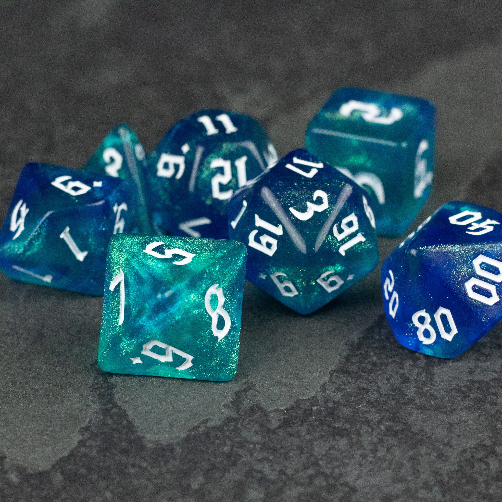 Blue & Green Glitter Dice Set - Set of blue and green glittery polyhedral dice with white numbering on dark textured surface.