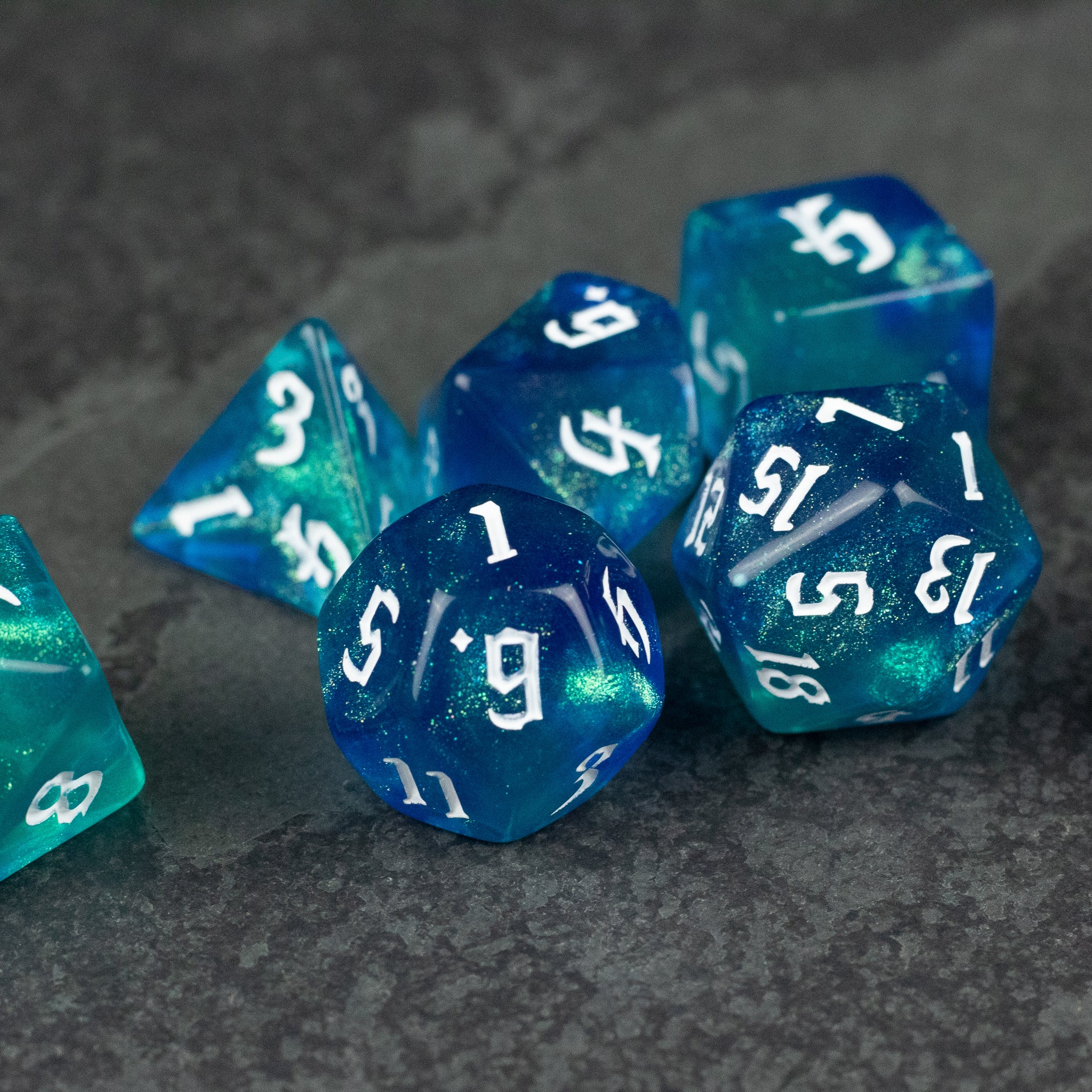 Blue & Green Glitter Dice Set - Set of blue and green glittery polyhedral dice with white numbering on a dark textured surface.