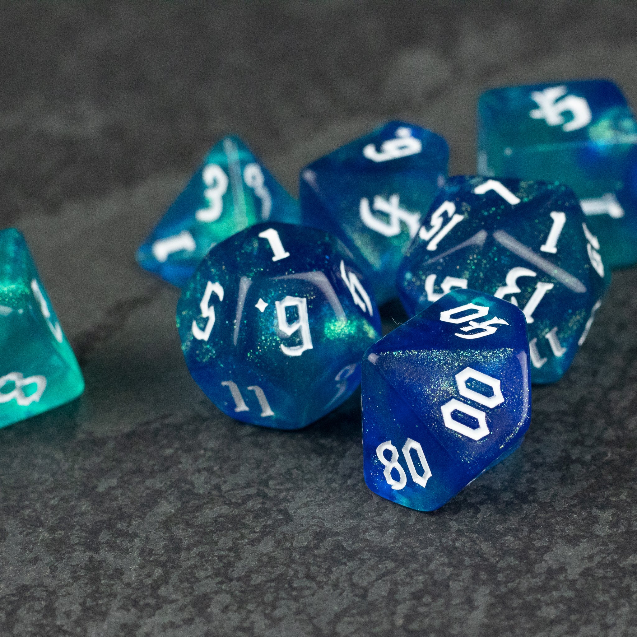 Blue & Green Glitter Dice Set - Set of blue and green glitter polyhedral dice with white numbering on dark textured surface.