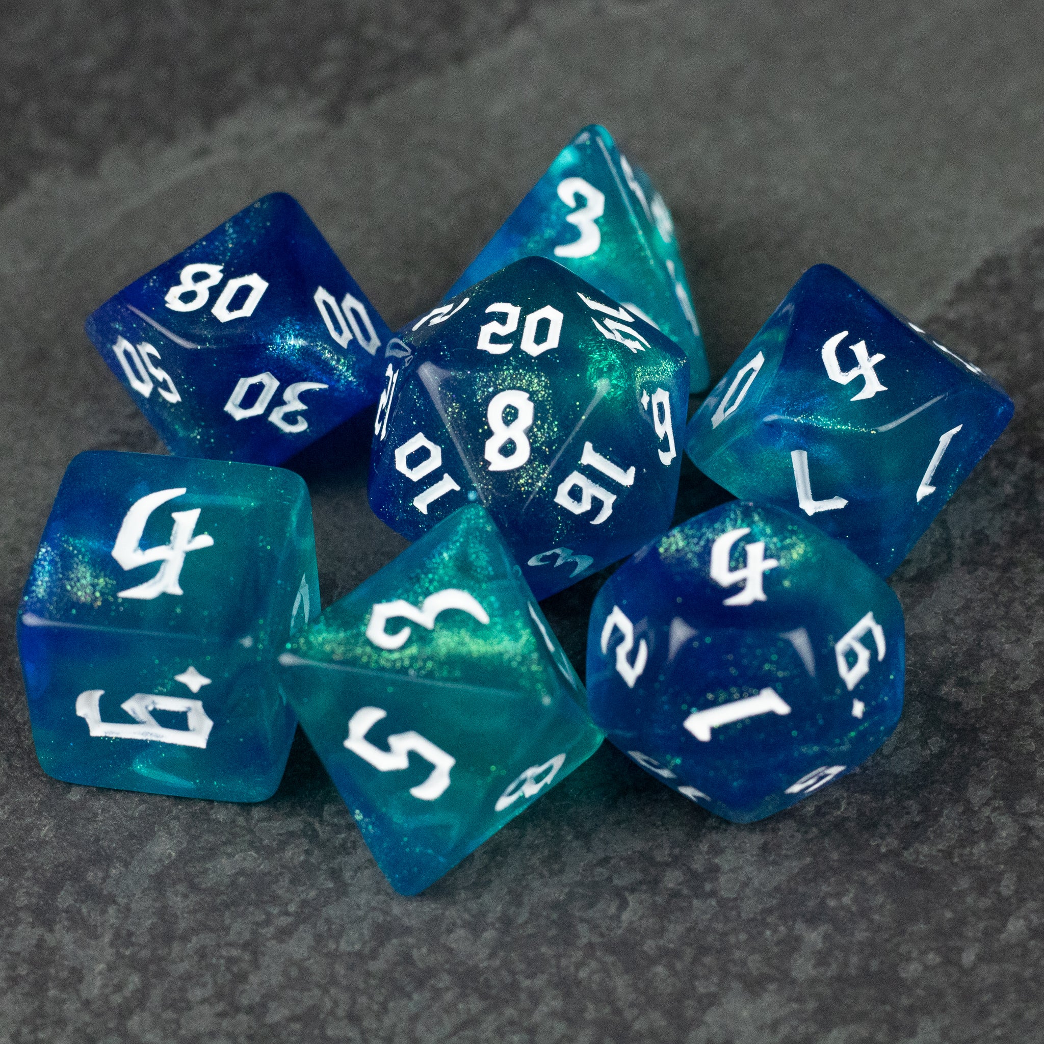 Blue & Green Glitter Dice Set - Set of seven polyhedral dice in blue and green glitter with white numbering, used for tabletop gaming.