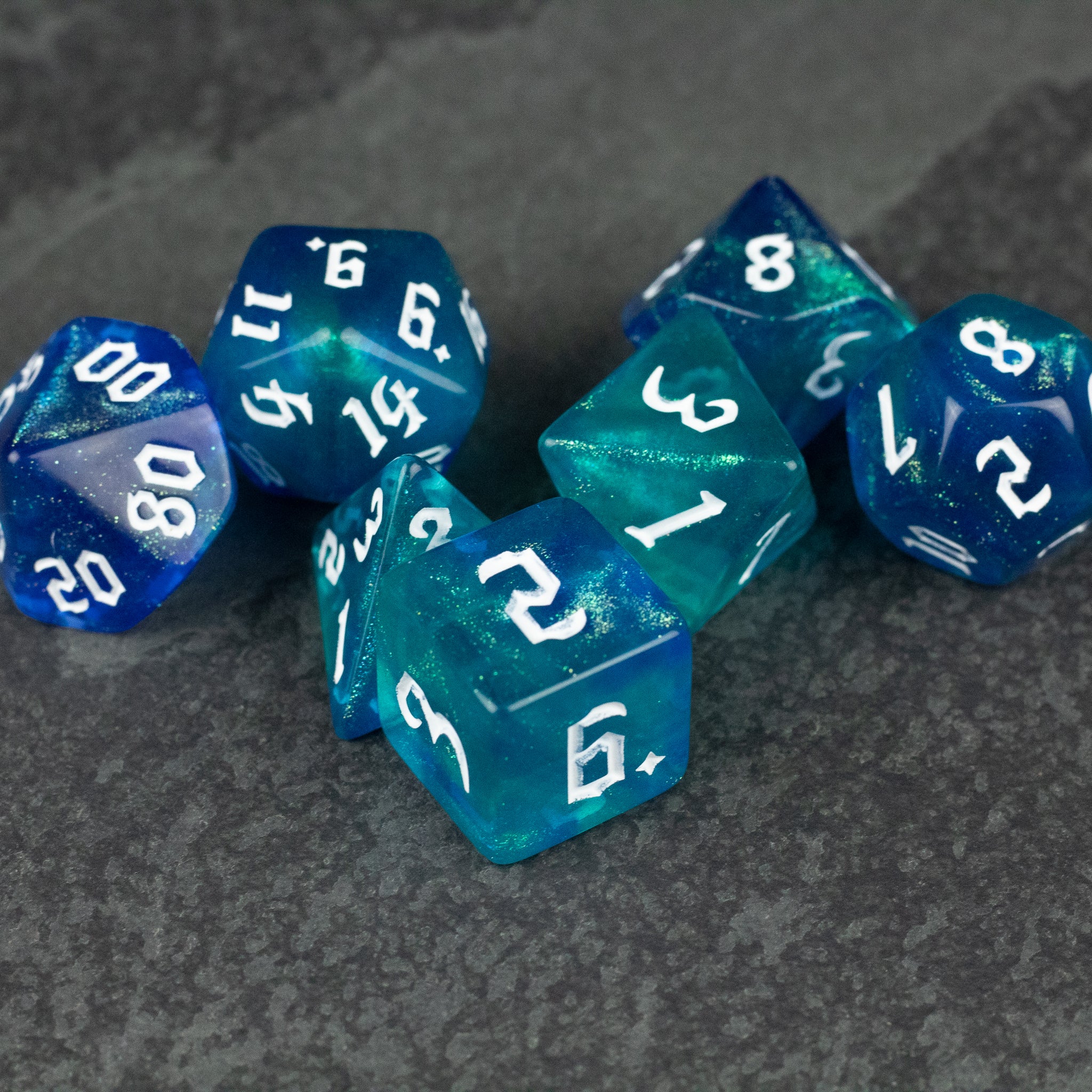 Blue & Green Glitter Dice Set - Set of translucent blue and green glitter polyhedral dice with white numbers on a gray surface.