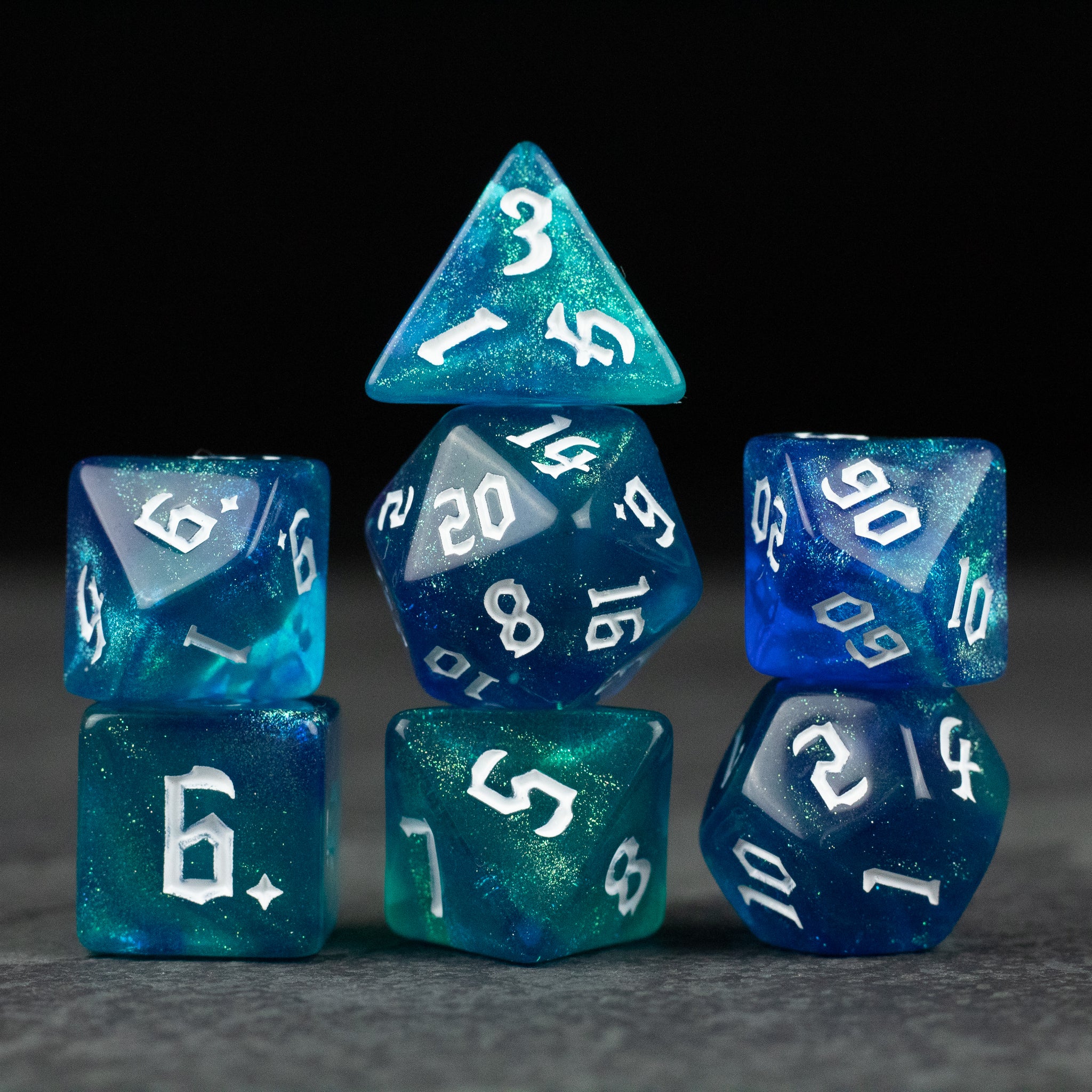 Blue & Green Glitter Dice Set - Set of seven translucent blue and green glitter dice with white numbers, including d4, d6, d8, d10, d12, and d20 shapes.