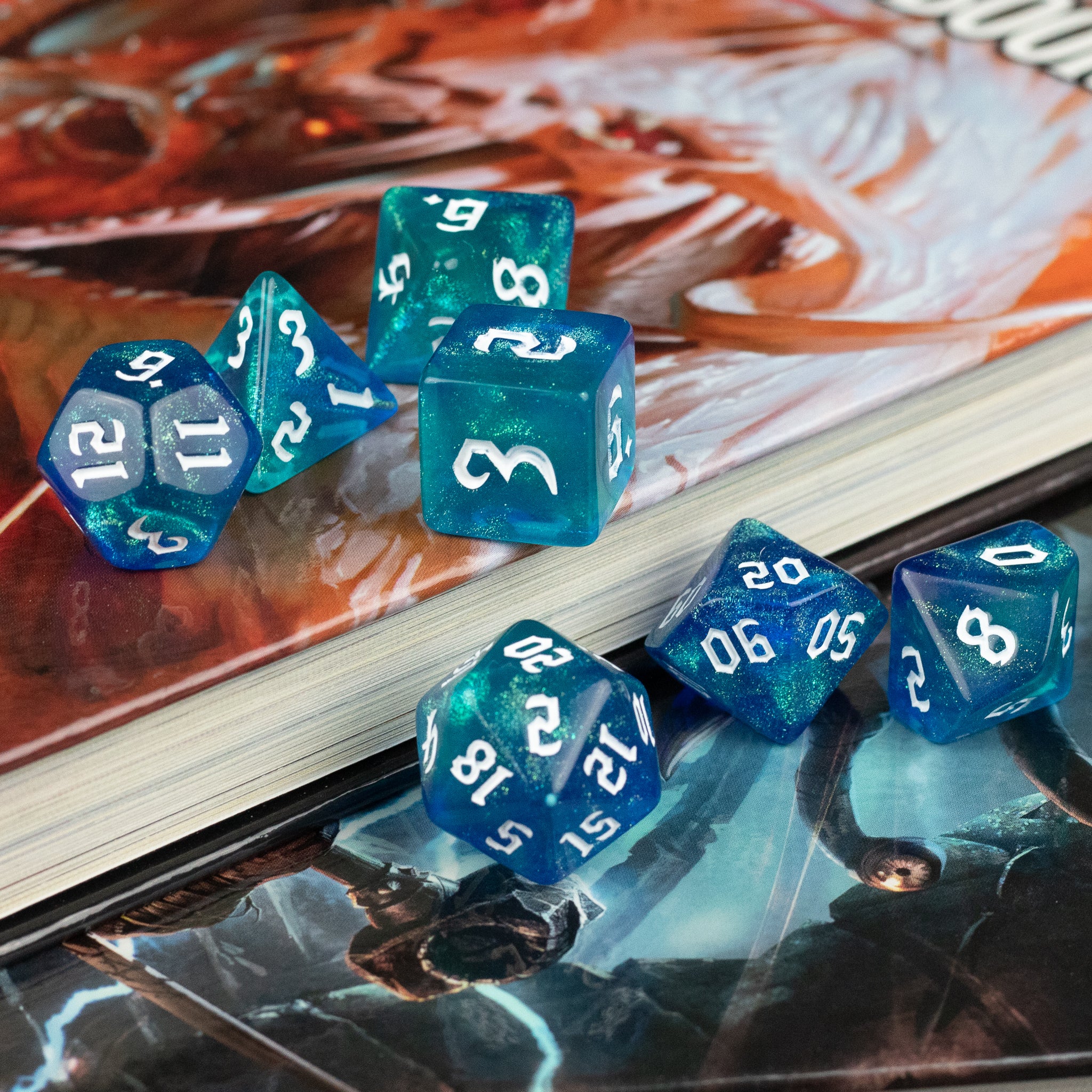 Blue & Green Glitter Dice Set - Blue and green glitter polyhedral dice set with various shapes on a game book background.
