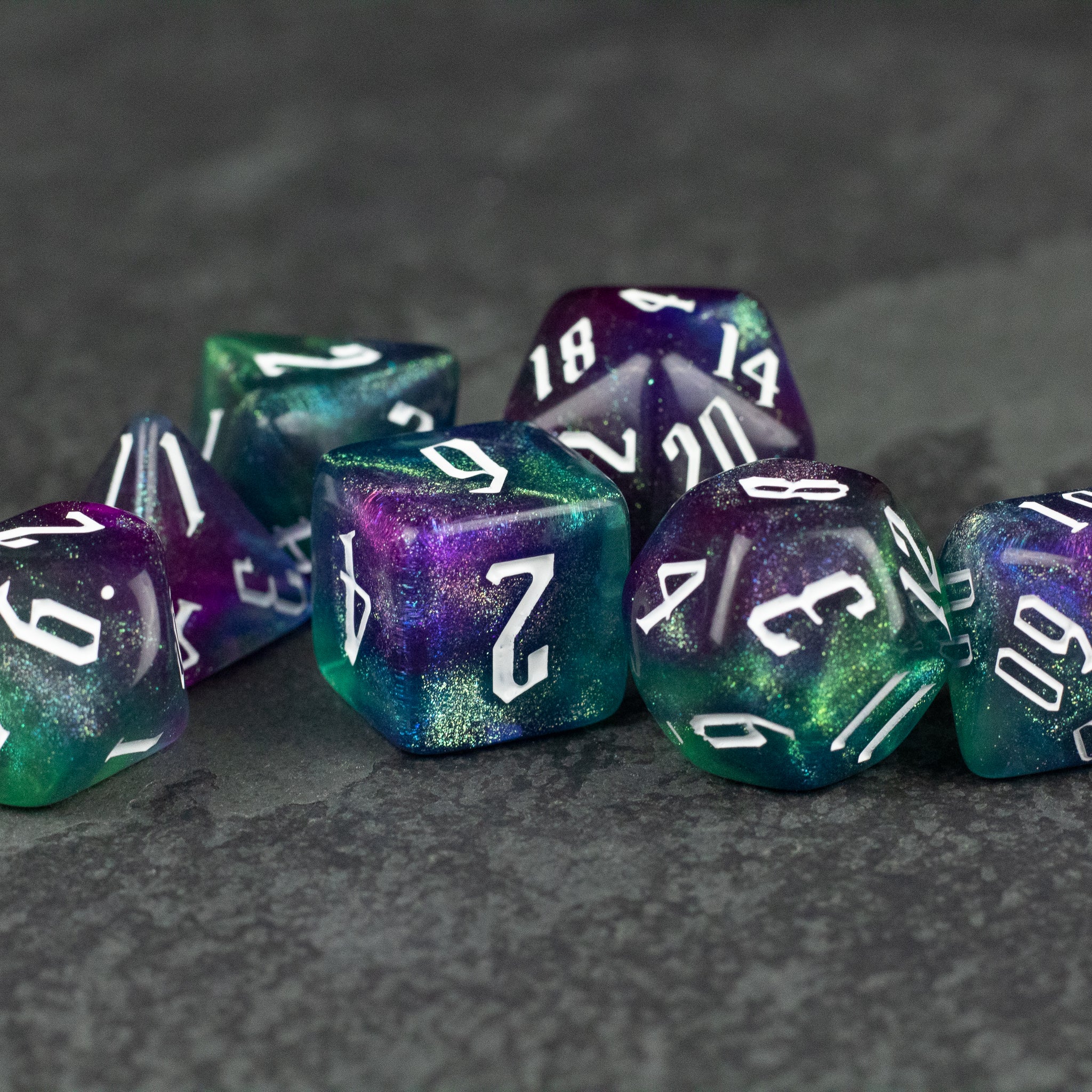 Purple & Green Glitter Dice Set - Set of purple and green glittery polyhedral dice with white numbering on a dark textured surface.