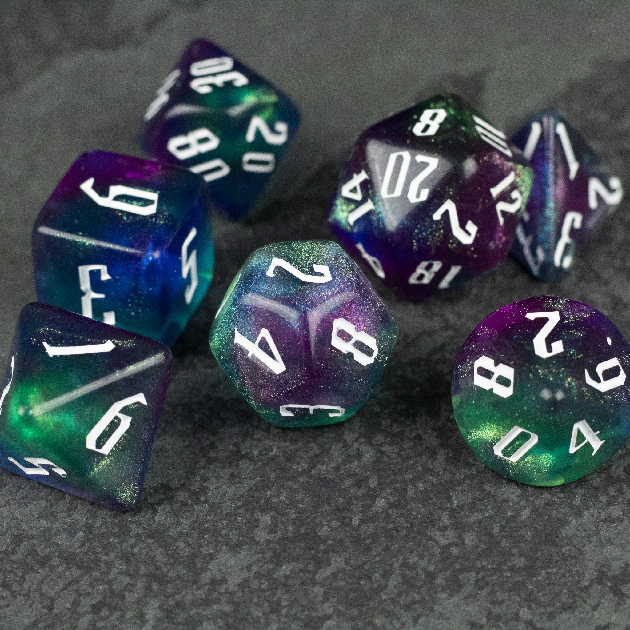 Purple & Green Glitter Dice Set - Set of purple and green glittery polyhedral dice with white numbers on a dark stone surface.
