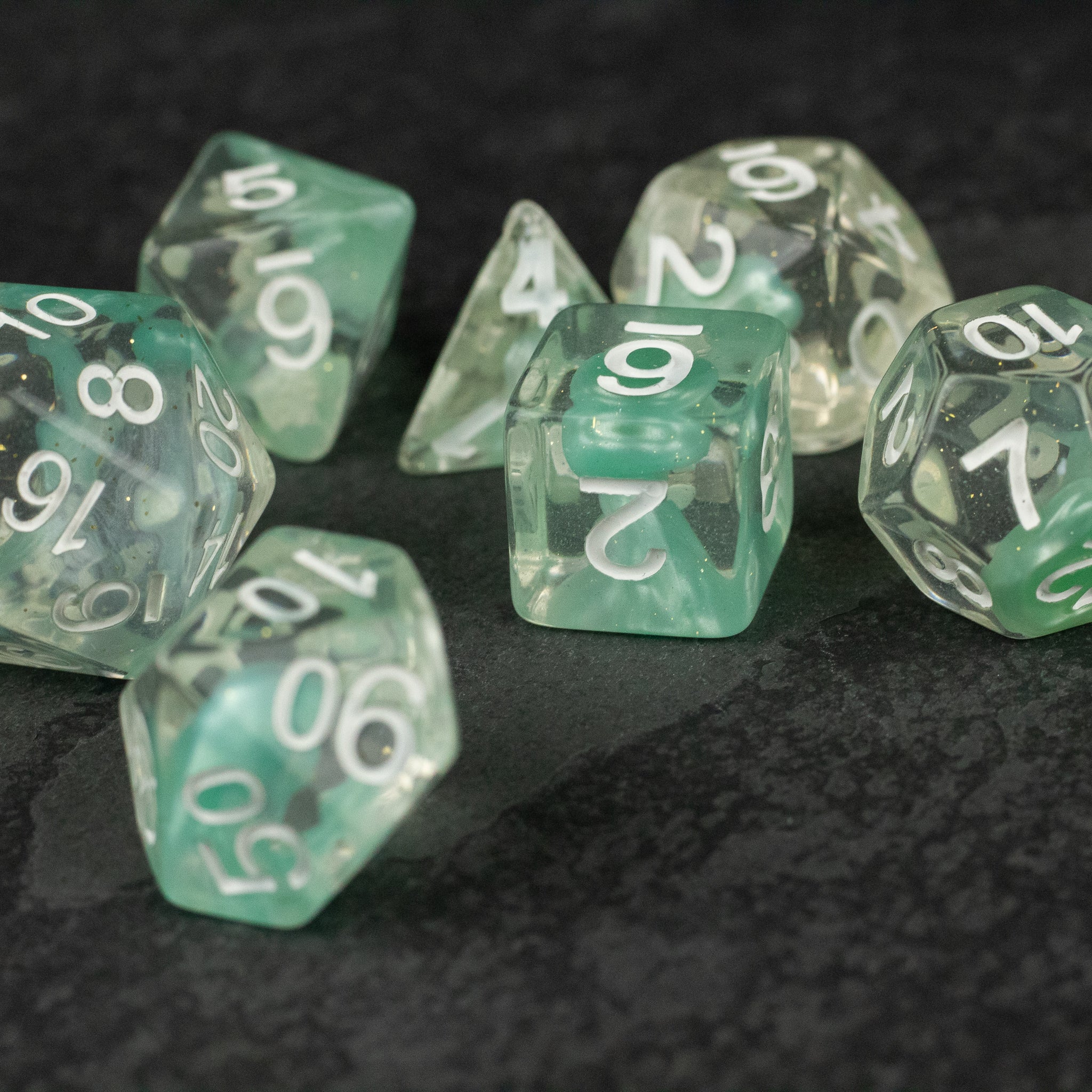 Cyan Lava Lamp Dice Set - Set of translucent cyan and clear polyhedral dice with white numbering on dark textured surface.