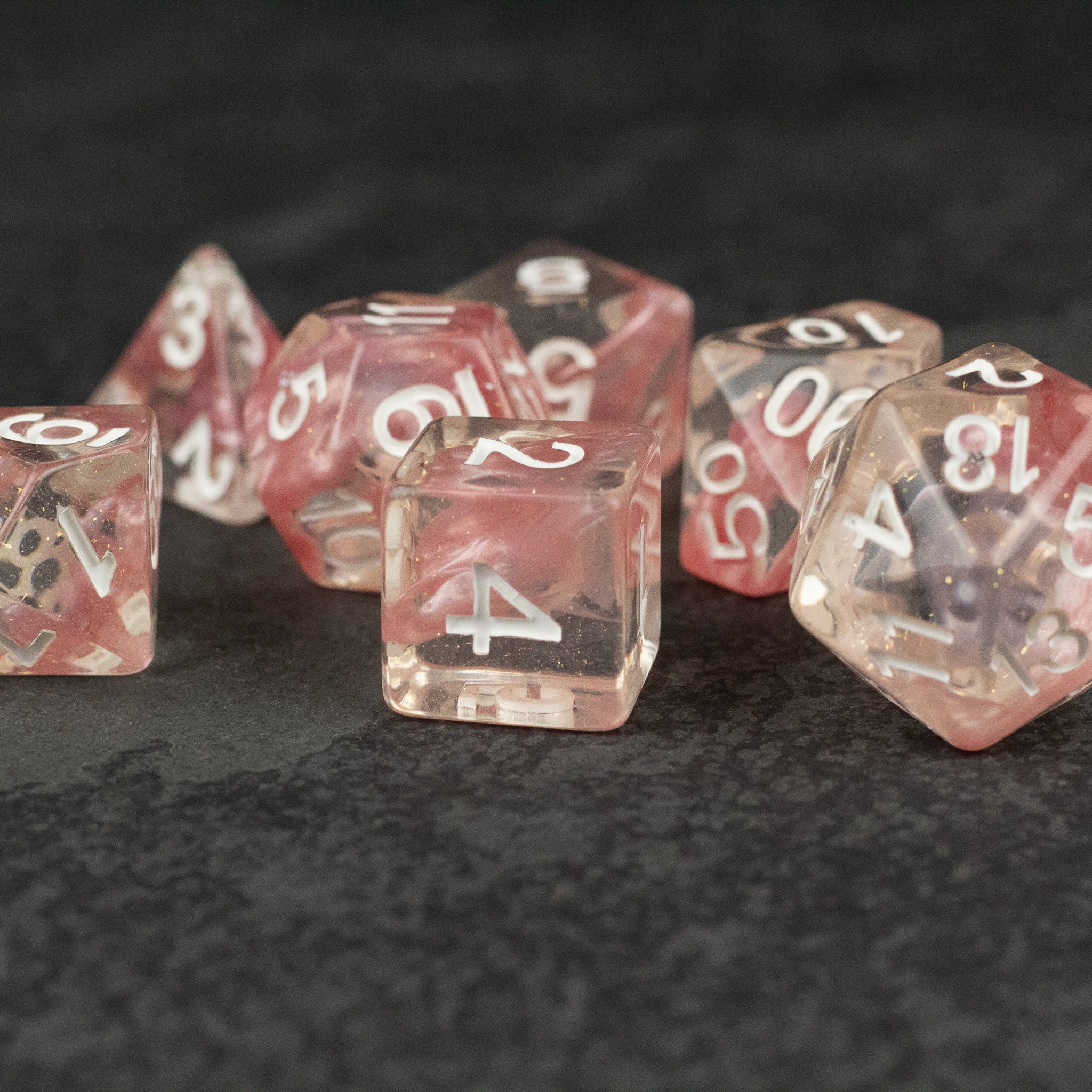 Pink Lava Lamp Dice Set - Translucent pink lava lamp style polyhedral dice set with white numbering on black surface.