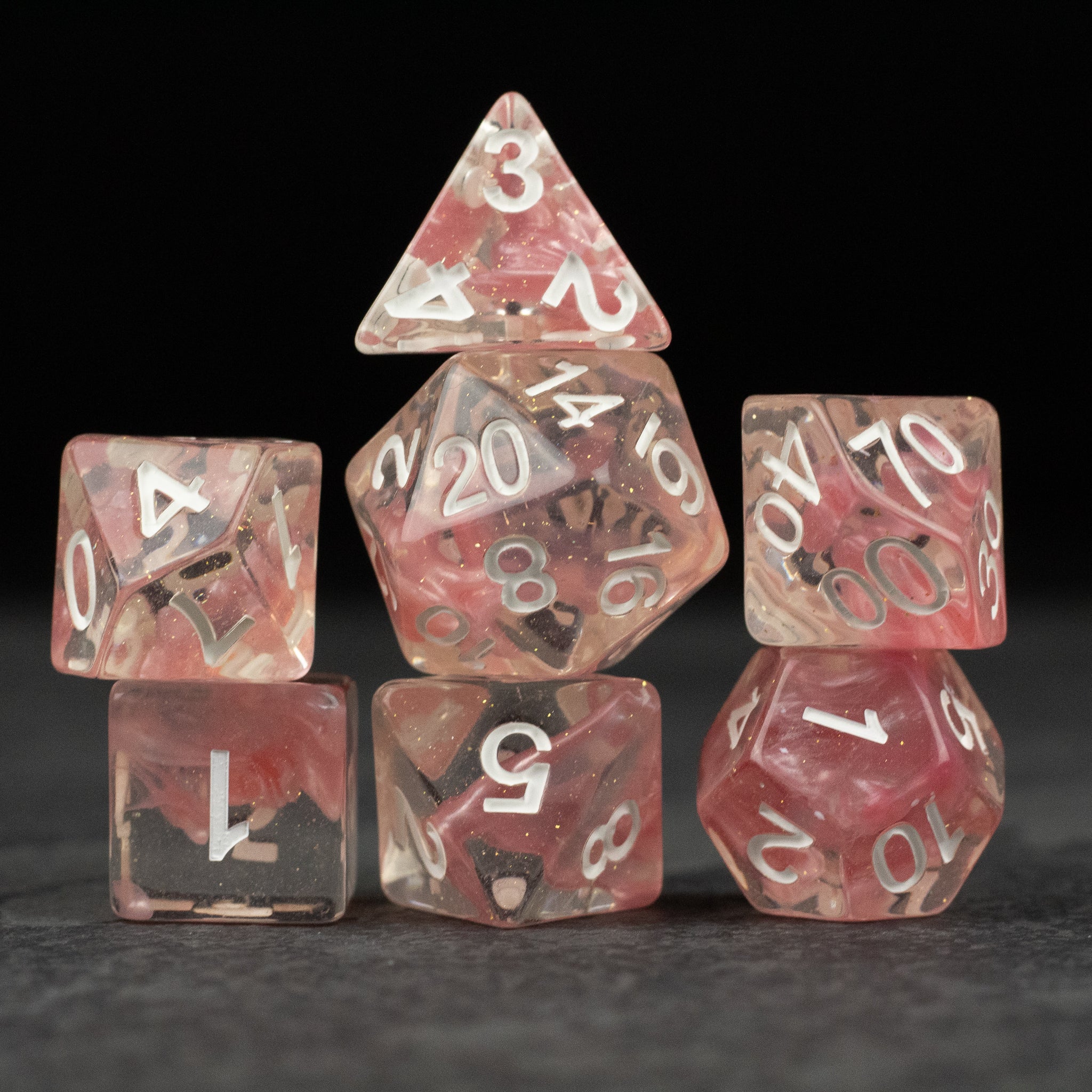 Pink Lava Lamp Dice Set - Seven translucent pink dice with white numbering, featuring a marbled lava lamp effect and varying shapes including a d20,.