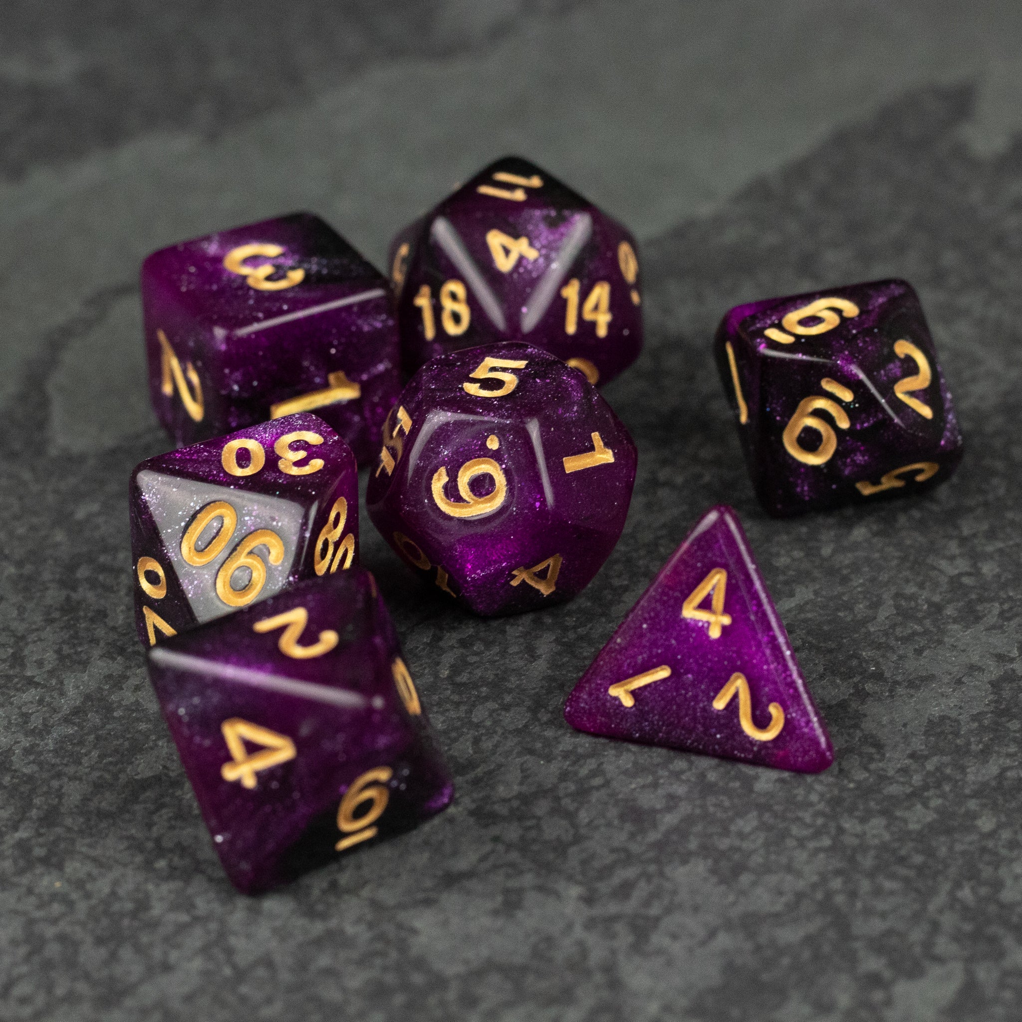 Purple and Black Glitter Dice Set - Seven purple and black glitter dice with gold numbers, including d20, d12, d10, d8, d6, and d4, on dark surface.
