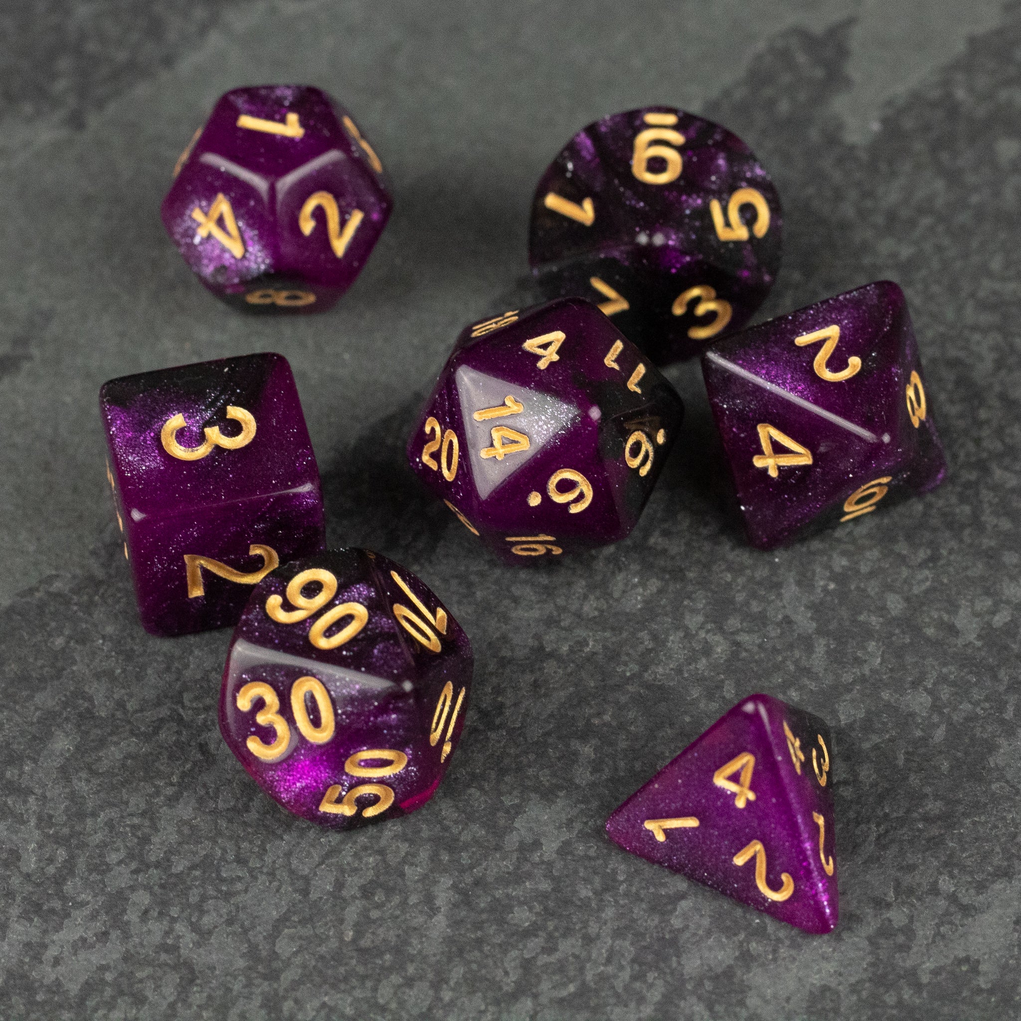 Purple and Black Glitter Dice Set - Seven purple and black glitter polyhedral dice with gold numbers on gray stone background.