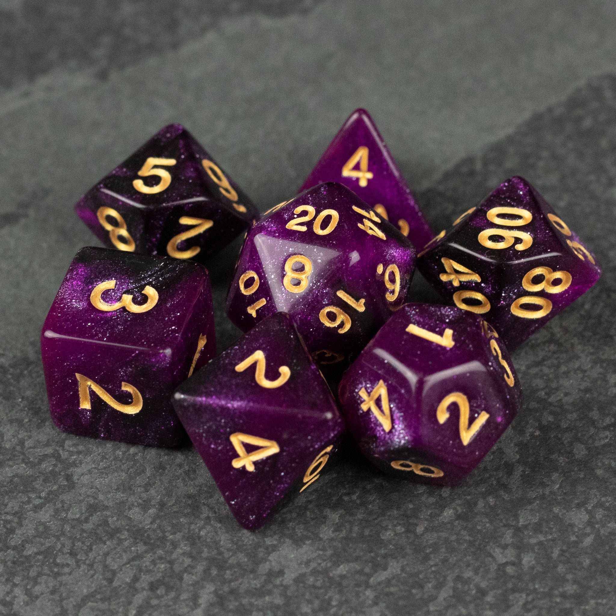 Purple and Black Glitter Dice Set - Set of purple and black glittery polyhedral dice with gold numbers on a dark surface.