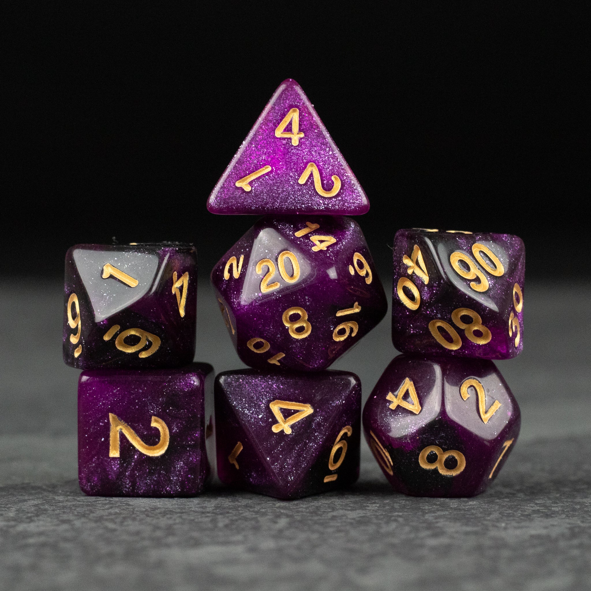 Purple and Black Glitter Dice Set - Purple and black glitter seven-piece dice set with gold numbers on gray surface.