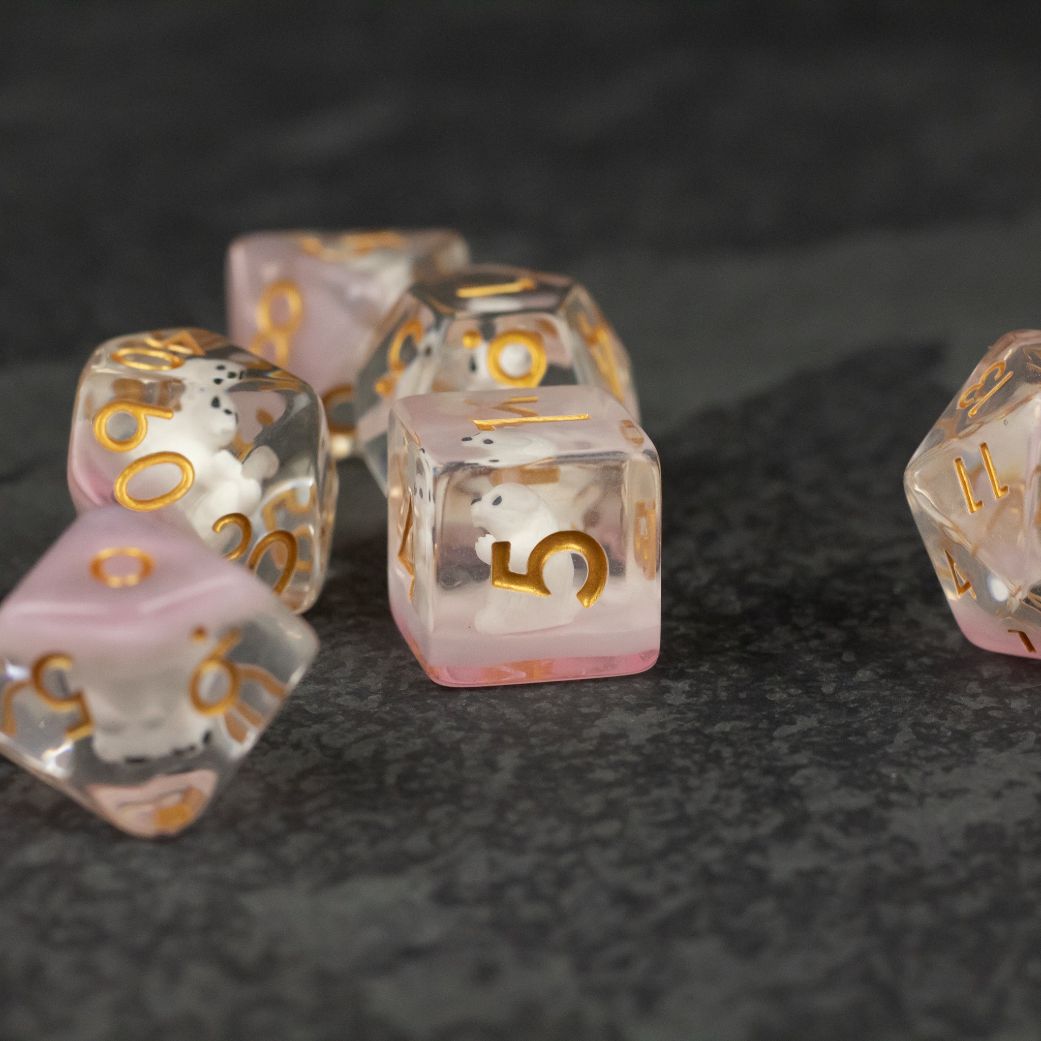Polar Bear Dice Set - Transparent dice set with white and soft pink swirls and gold numbers on a dark textured surface.