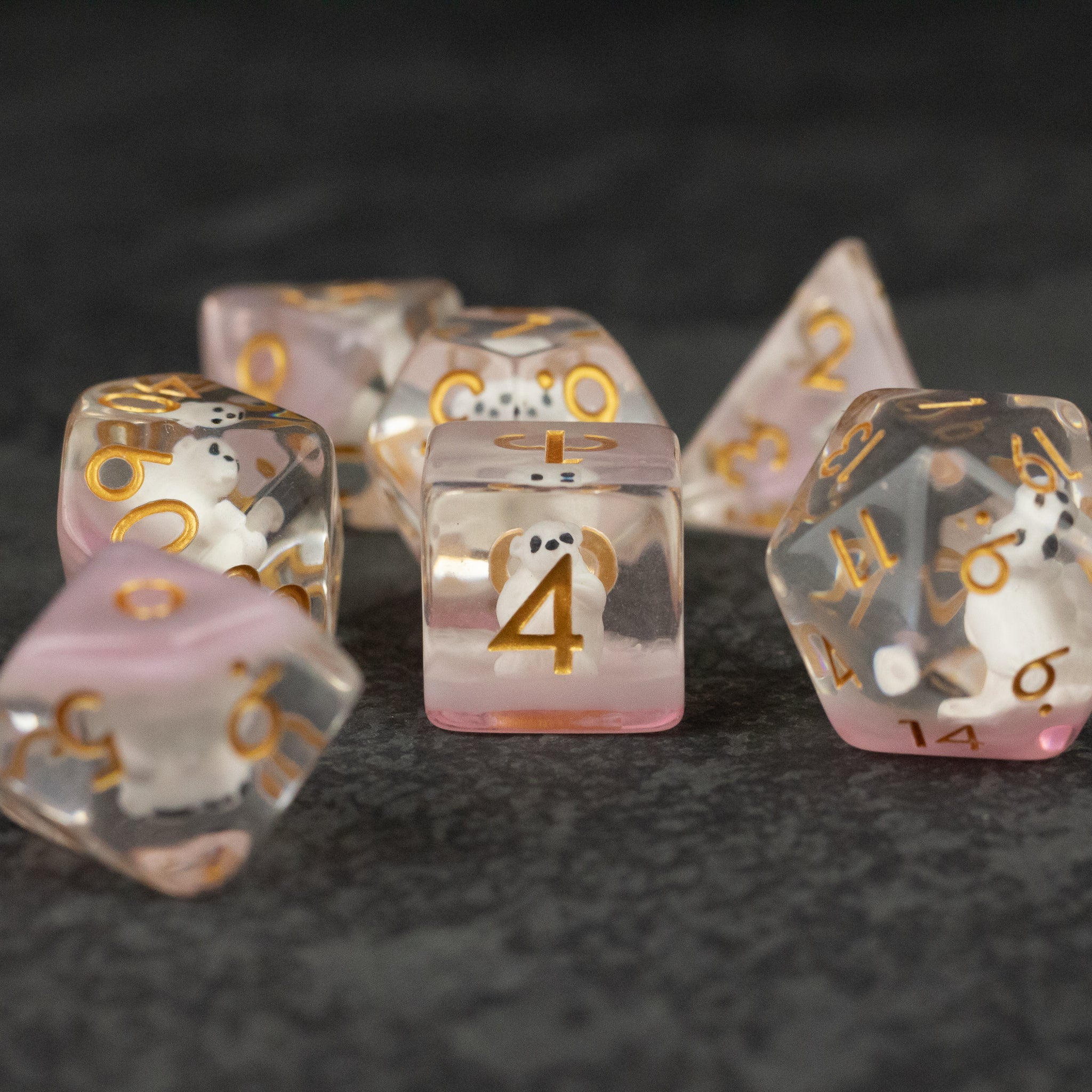 Polar Bear Dice Set - Set of translucent white and pink polyhedral dice with gold numbers on a dark textured surface.