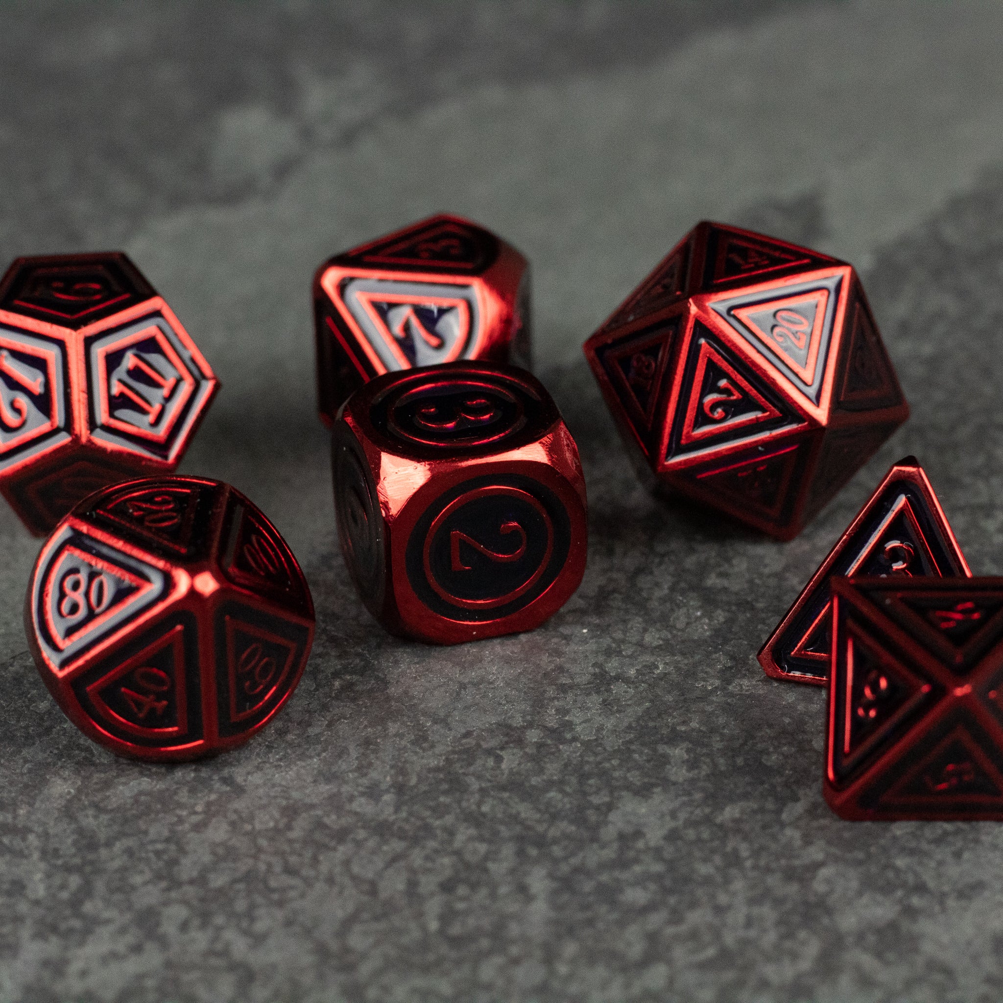 Crimson Ritual Dice Set - Red metal polyhedral dice set with black engraved numbers on a dark stone surface.