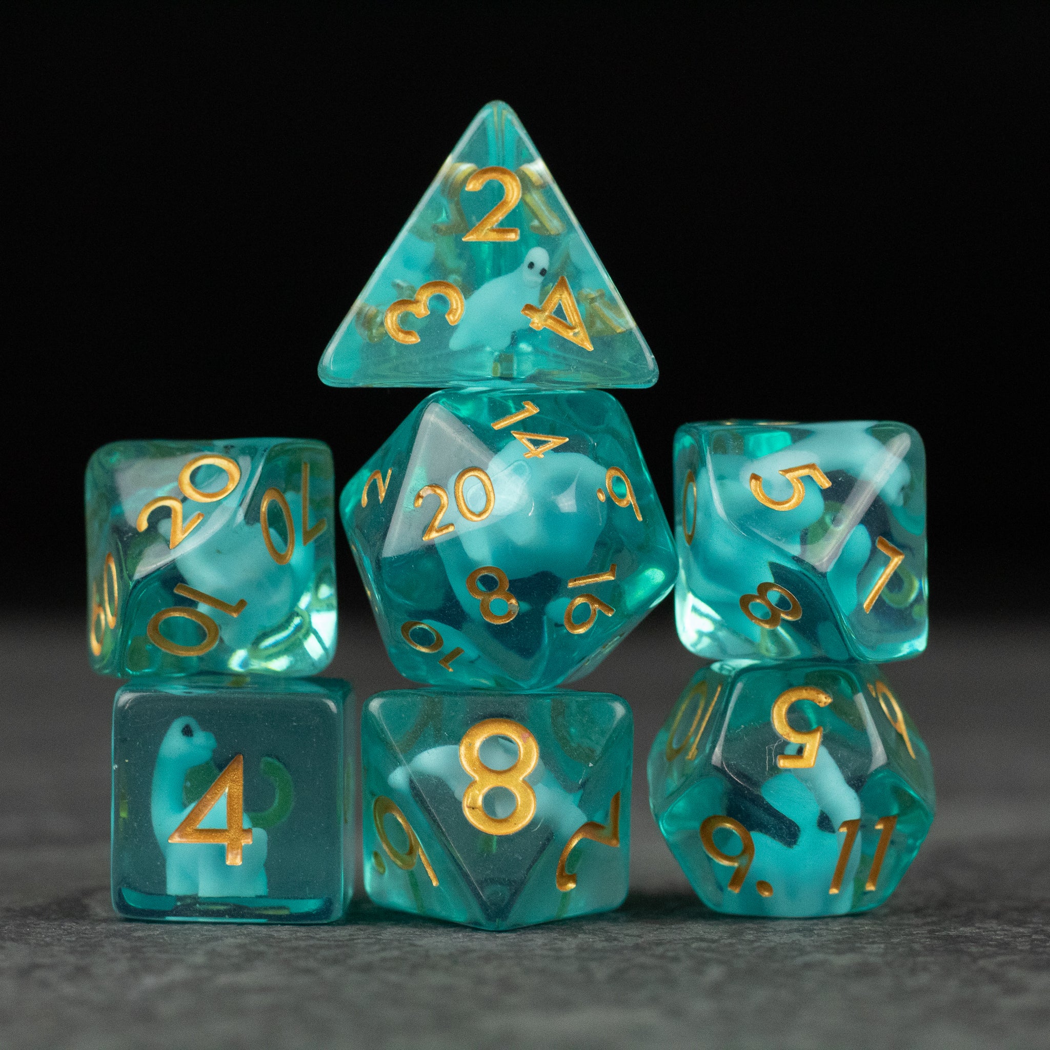 Blue Brontosaurus Dice Set - Translucent teal seven-piece polyhedral dice set with gold numbering, including d20, d12, d10, d8, d6, d4, and percentile.