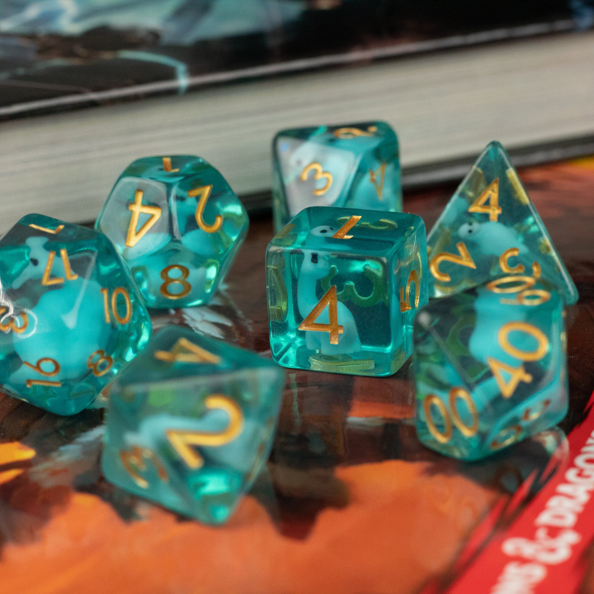Blue Brontosaurus Dice Set - Blue translucent polyhedral dice set with gold numbers, featuring various shapes including a large d20 and a d6 cube.
