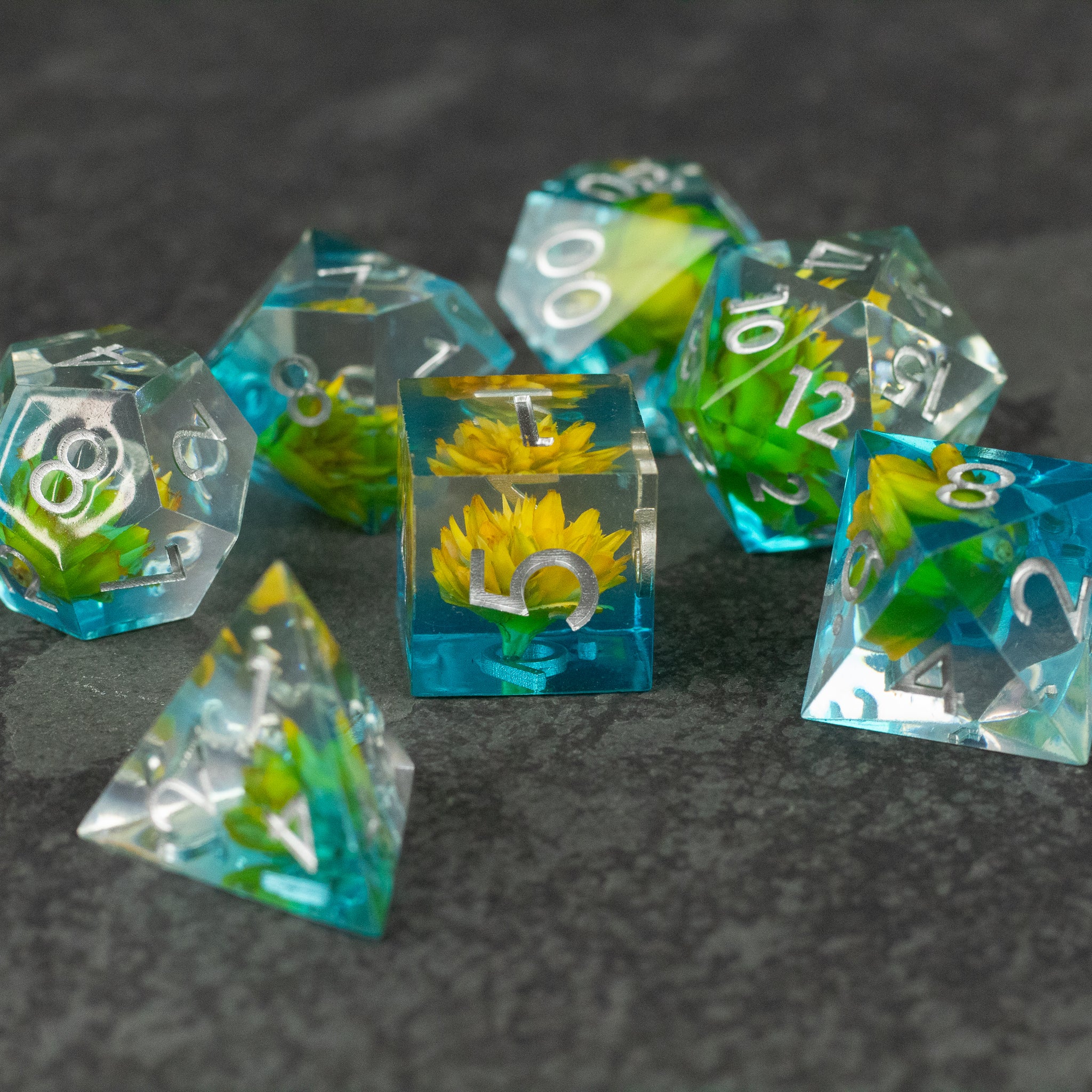 Yellow Flower + Blue Resin Sharp Edge Dice Set - Set of sharp edge polyhedral dice with blue resin and embedded yellow flowers, white numbering.