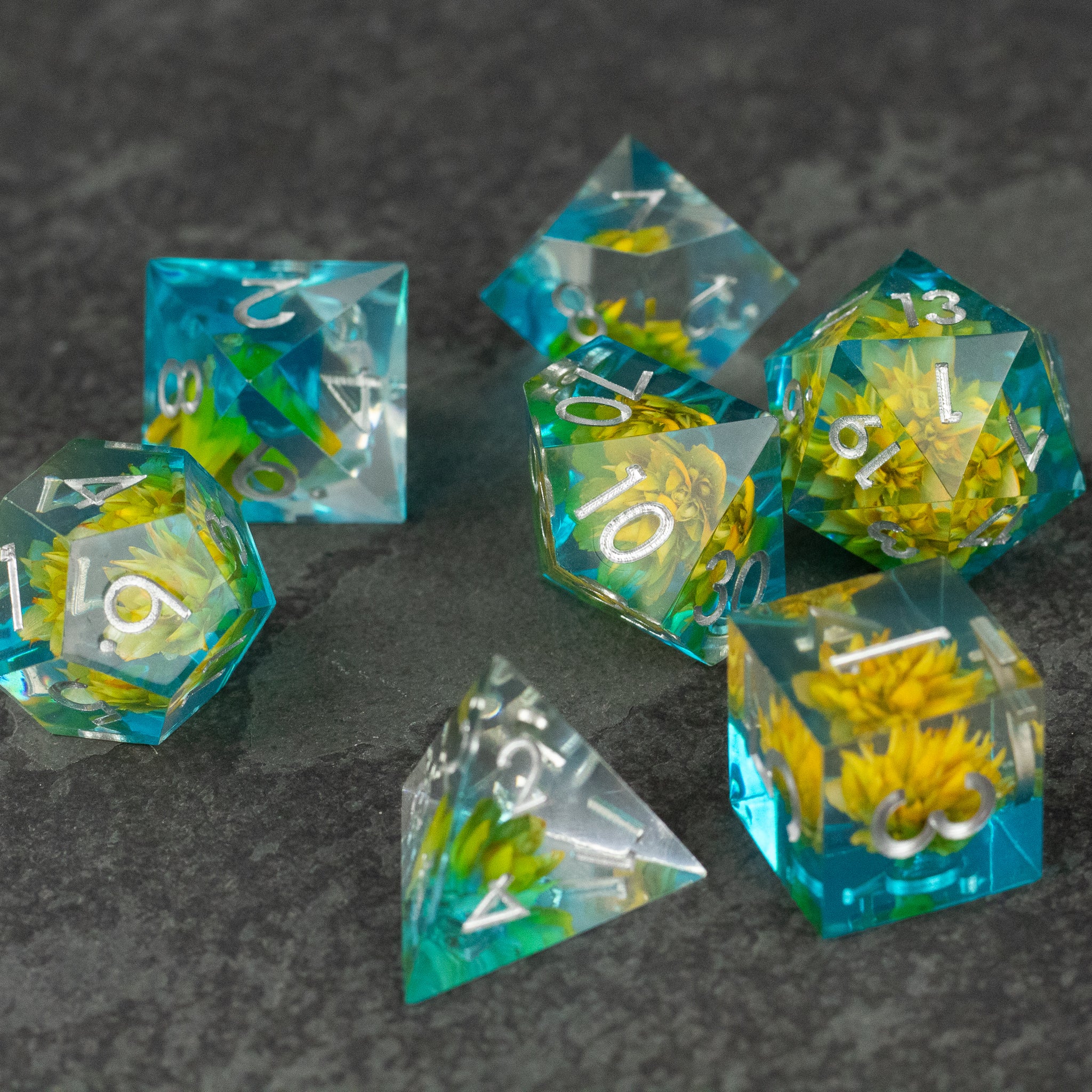 Yellow Flower + Blue Resin Sharp Edge Dice Set - Set of sharp-edged translucent blue resin dice with embedded yellow flowers and white numbering.