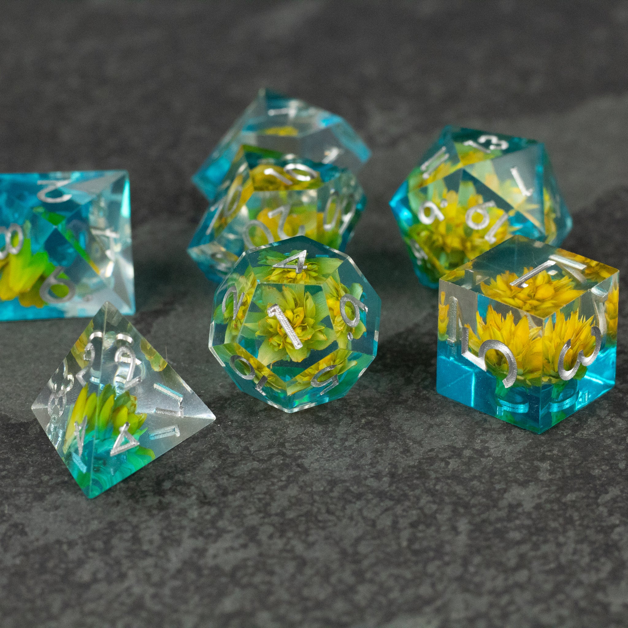 Yellow Flower + Blue Resin Sharp Edge Dice Set - Set of six sharp-edged translucent blue resin dice with embedded yellow flowers and white numbers.
