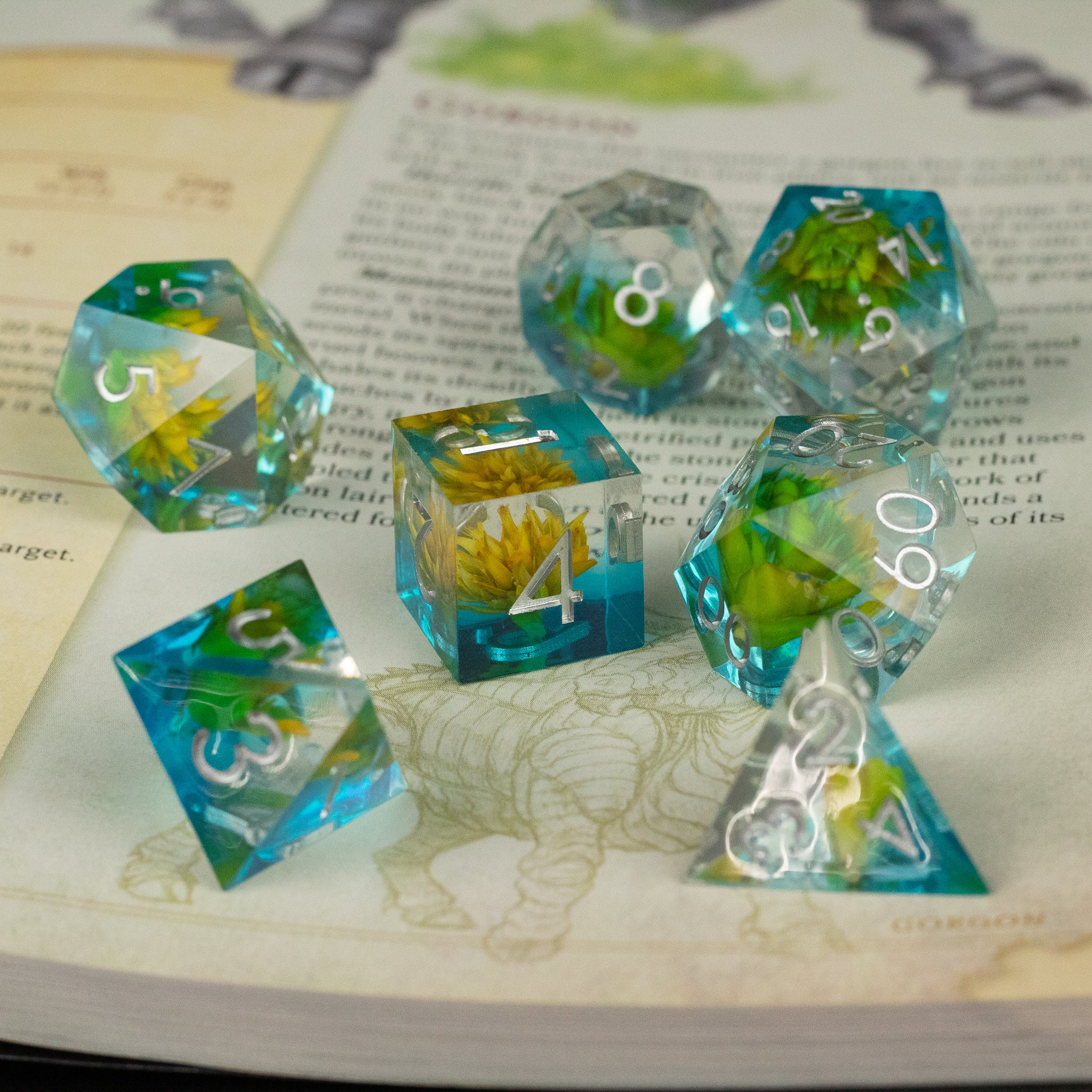 Yellow Flower + Blue Resin Sharp Edge Dice Set - Set of sharp edge polyhedral dice with clear blue resin and embedded yellow flowers, white numbering.