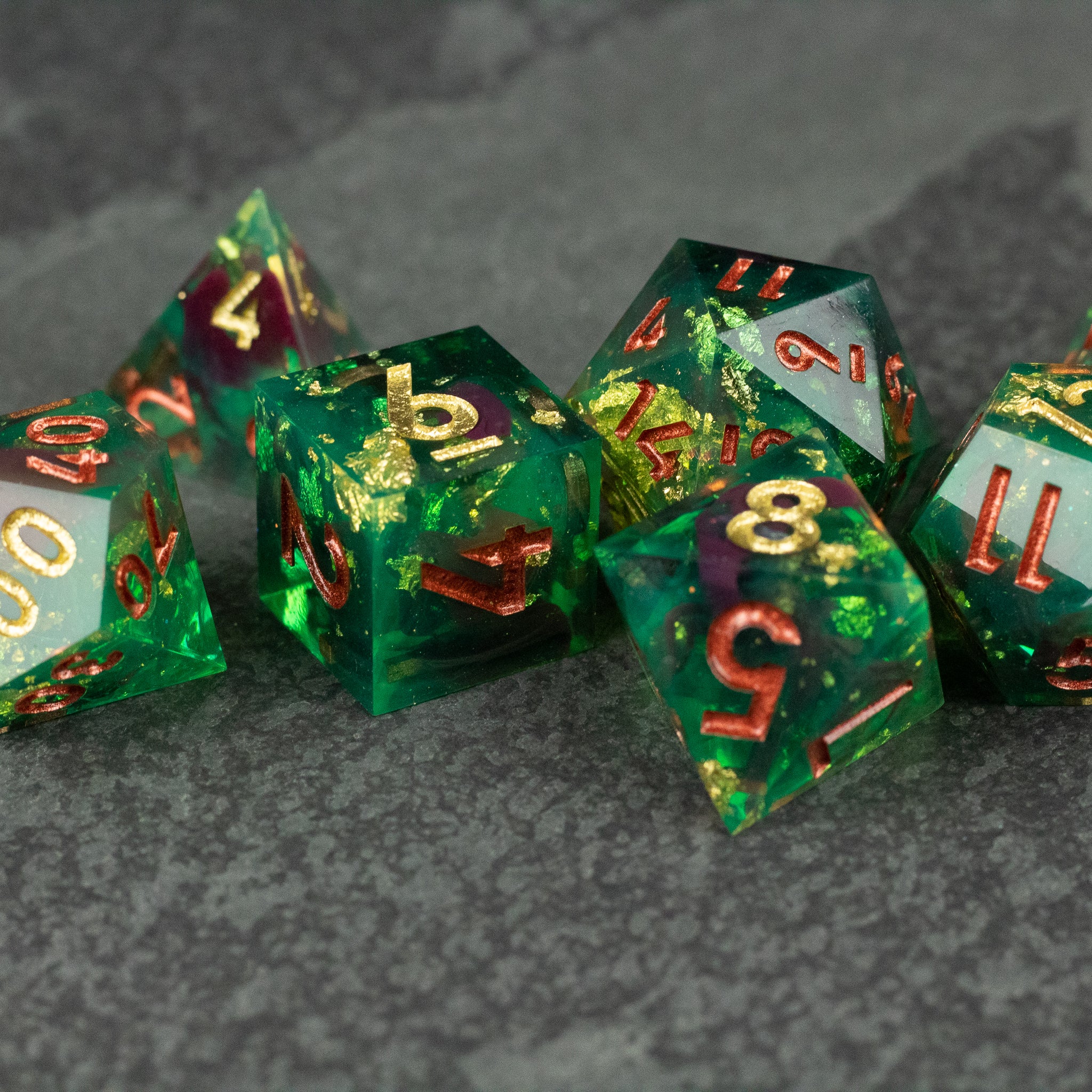 Primal Blood Dice Set - Green sharp-edged dice set with gold and red numbers on a textured gray surface.