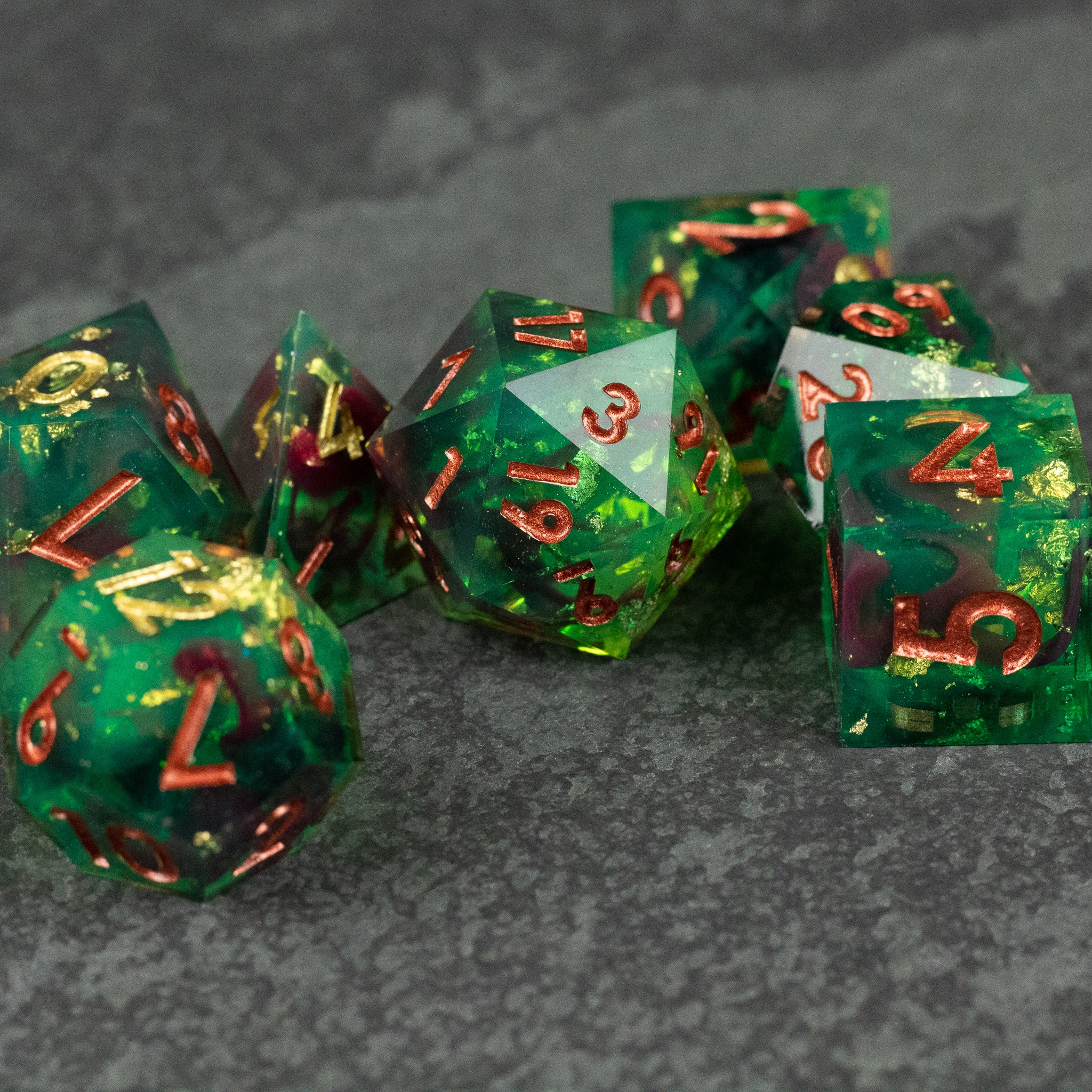 Primal Blood Dice Set - Sharp-edged green polyhedral dice set with red and gold numbering on dark stone surface.