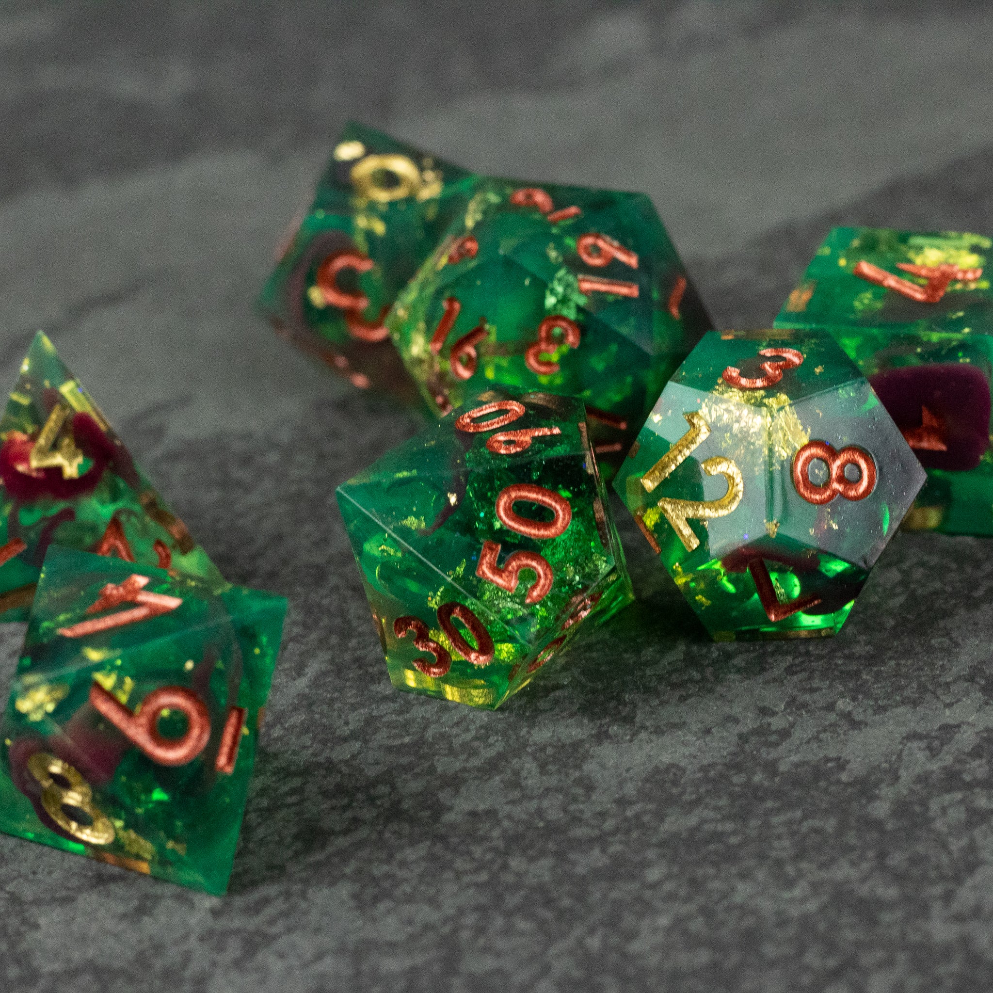 Primal Blood Dice Set - Green translucent polyhedral dice set with sharp edges and gold numbering on a dark surface.