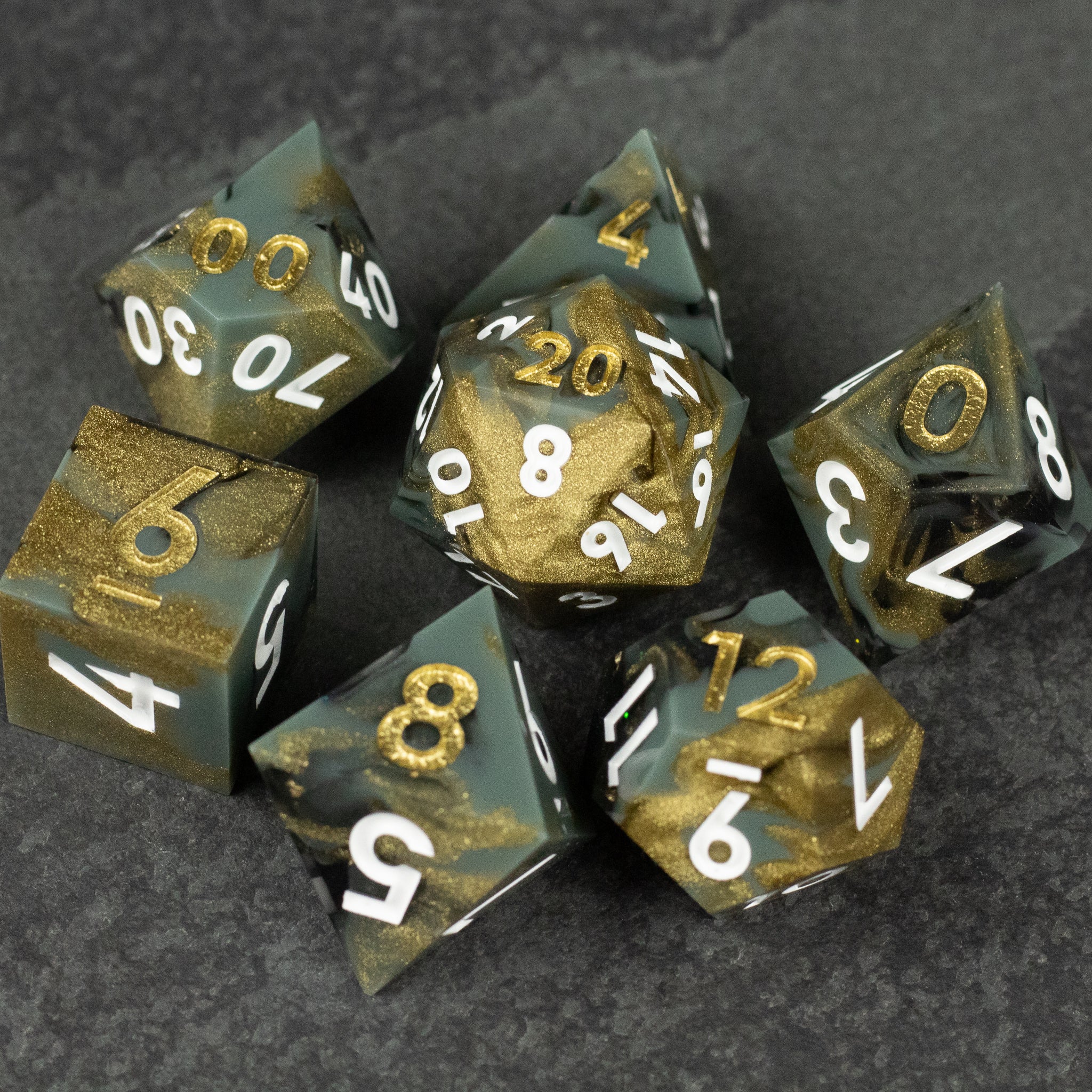 Greedfall Dice Set - Set of seven sharp-edged, black and gold marbled dice with white numbering on dark stone background.