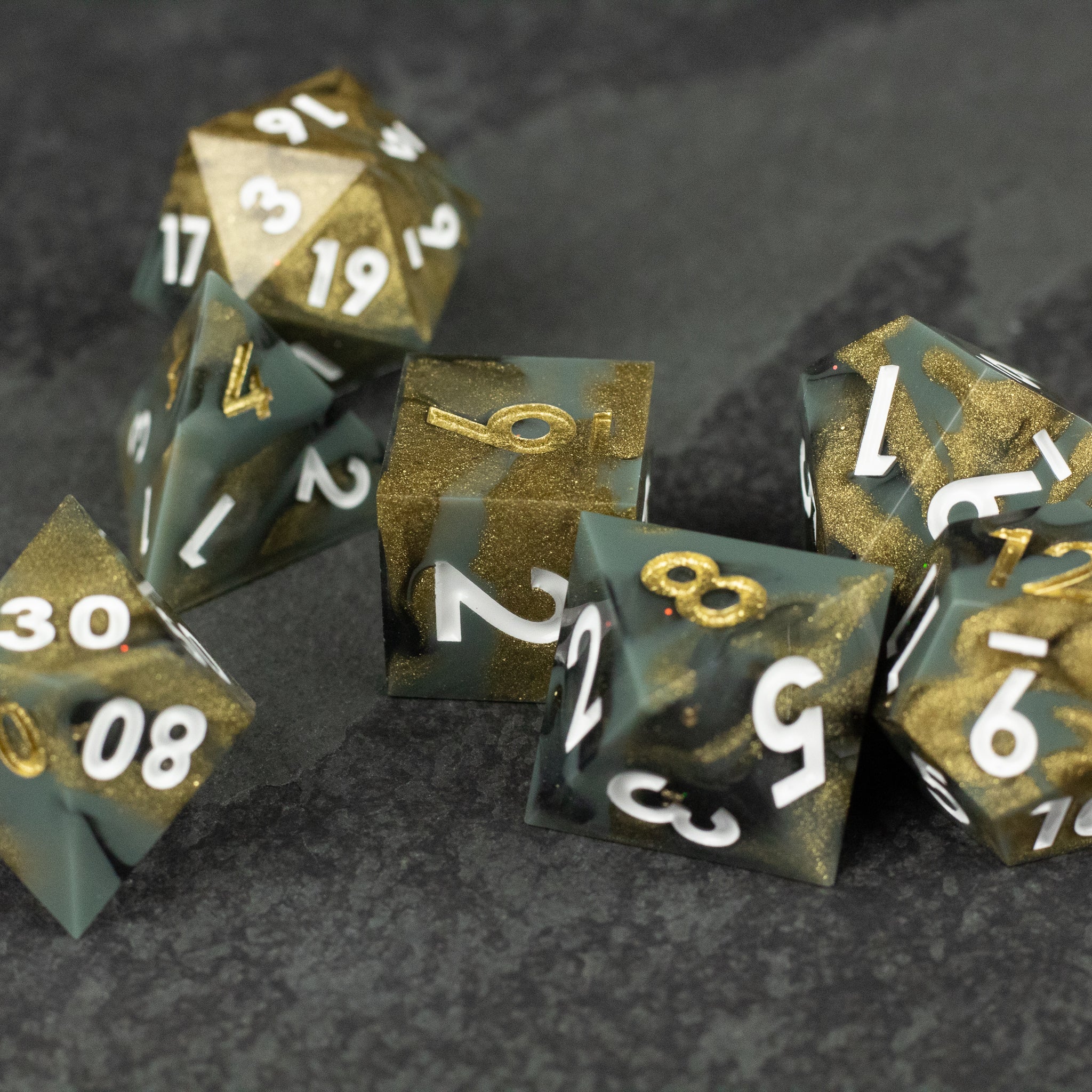 Greedfall Dice Set - Set of sharp-edged polyhedral dice in green and gold with white numbers on dark textured surface.