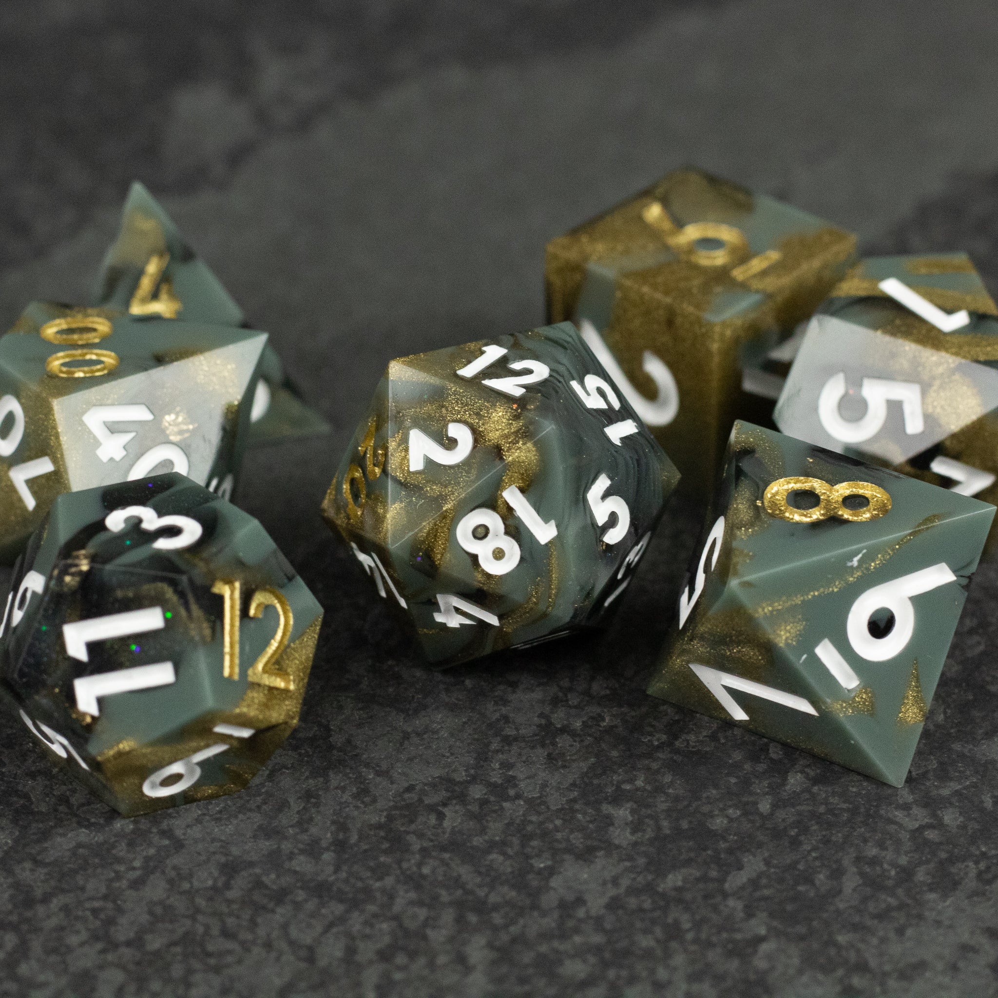 Greedfall Dice Set - Set of seven sharp-edged polyhedral dice with smoky transparent green and gold swirls, white and gold numbering.
