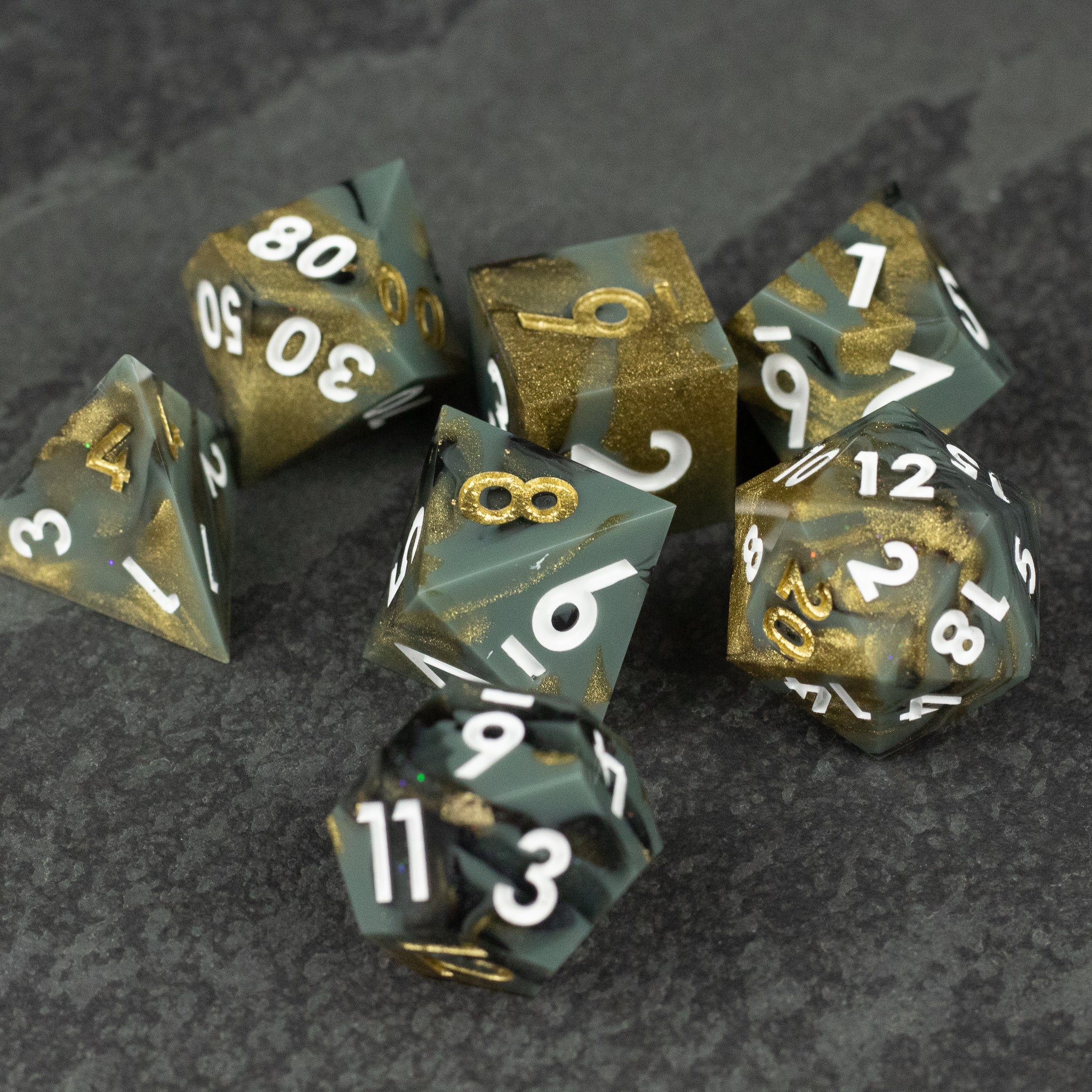 Greedfall Dice Set - Seven sharp-edged polyhedral dice in black and gold marbled resin with white numbers.