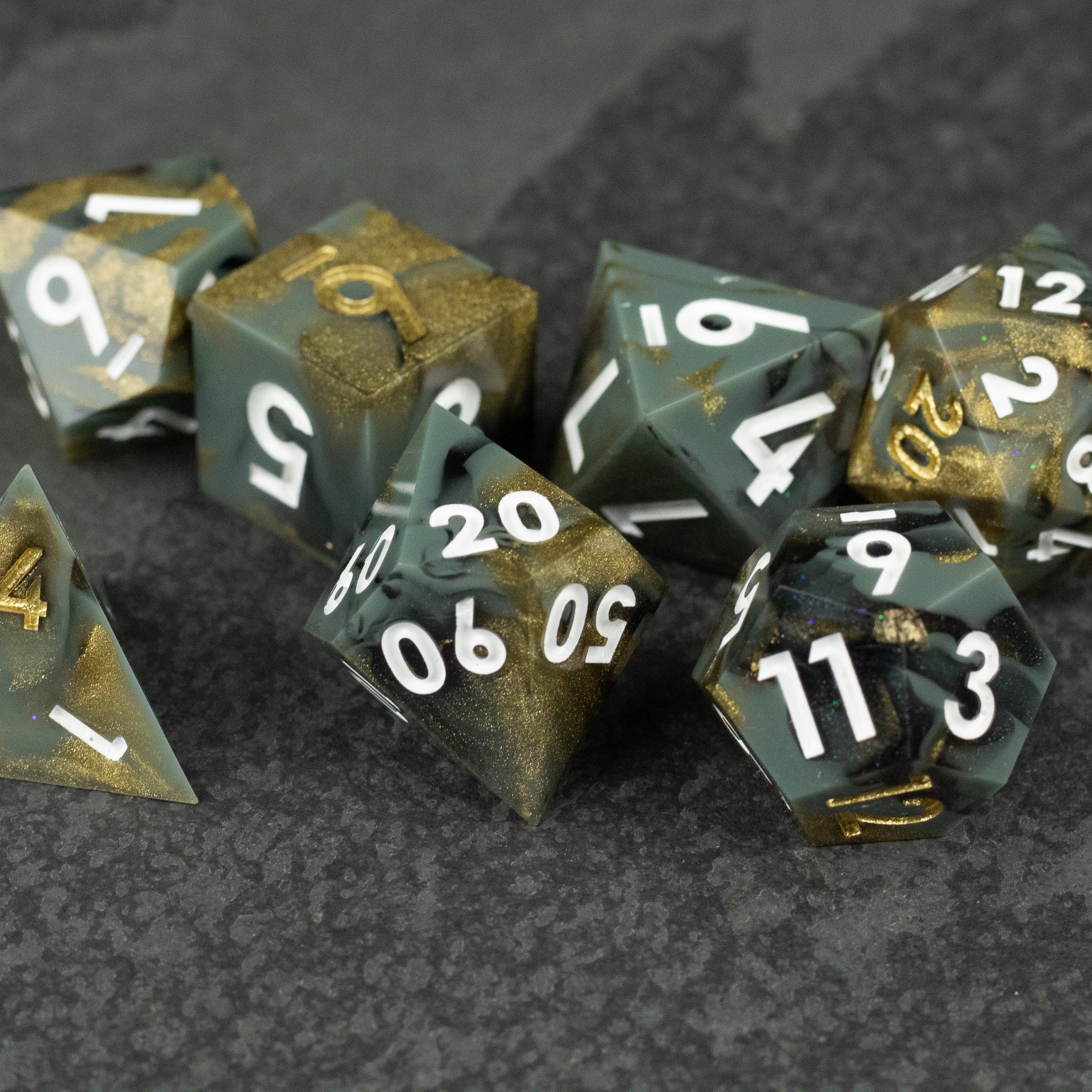 Greedfall Dice Set - Set of sharp-edged polyhedral dice in green and gold with white numbers on dark textured surface.