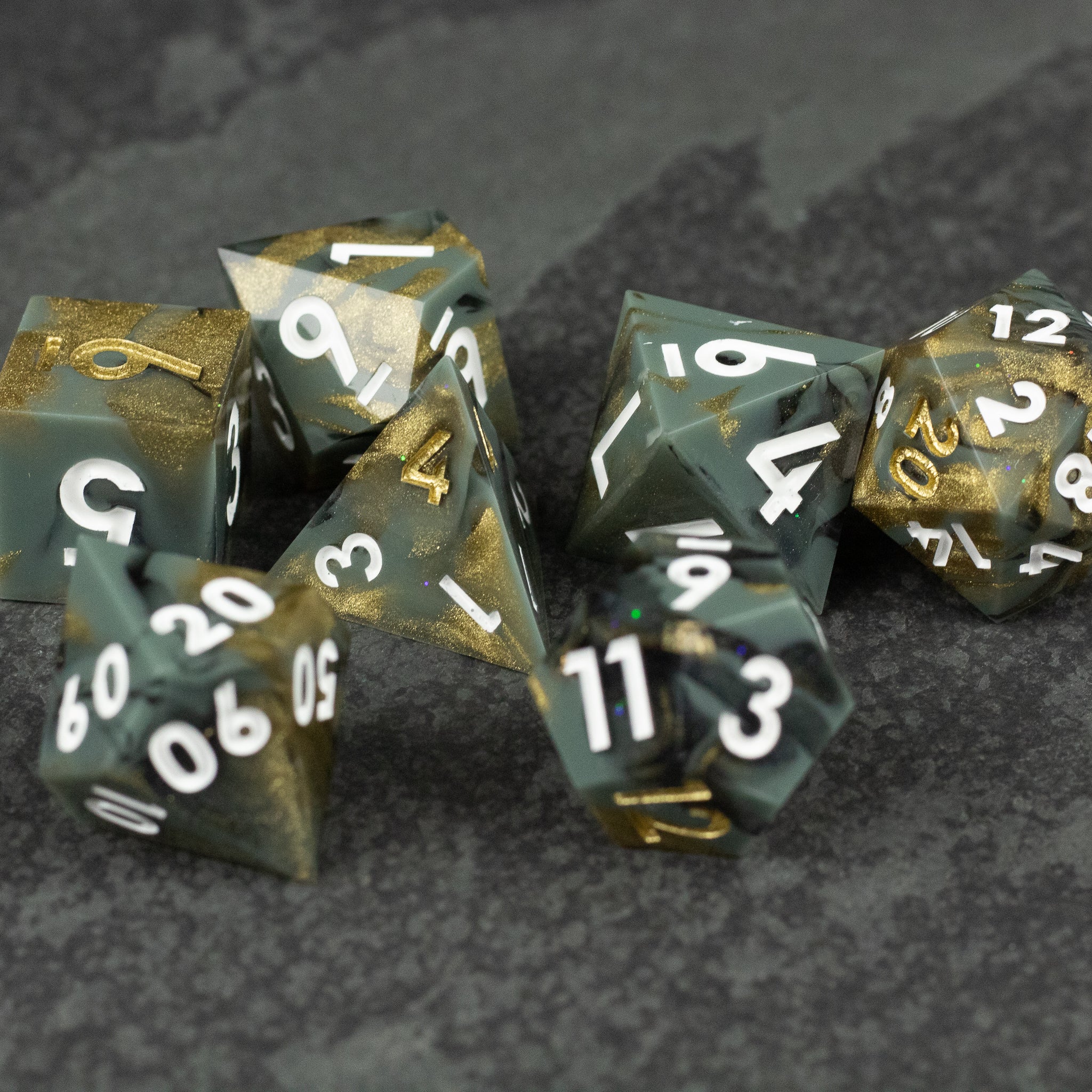 Greedfall Dice Set - Set of seven polyhedral dice with sharp edges, featuring mixed translucent green and gold tones with white and gold numbers.